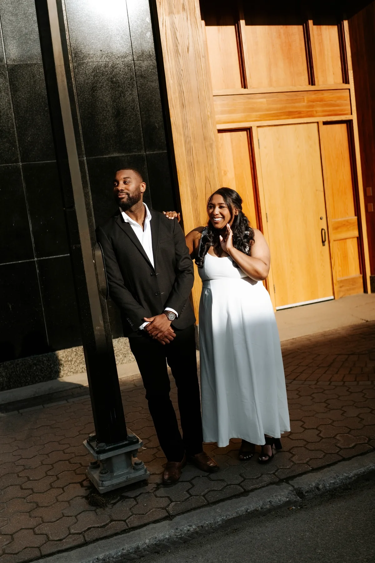 Jaida and Jordan laughing together against a marble pillar at the CMHR, downtown Winnipeg — wedding photography by Ngo Photography