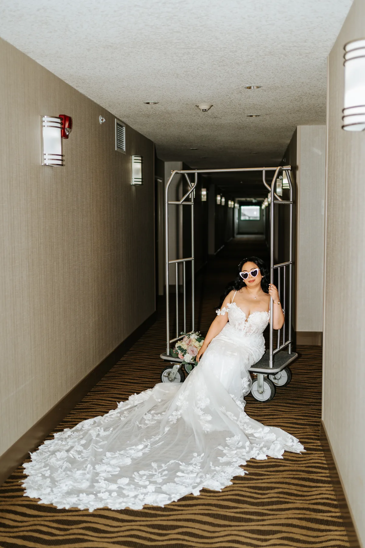 Jay in her wedding gown on a luggage cart in the hotel corridor — Hawthorne Estates wedding, Manitoba