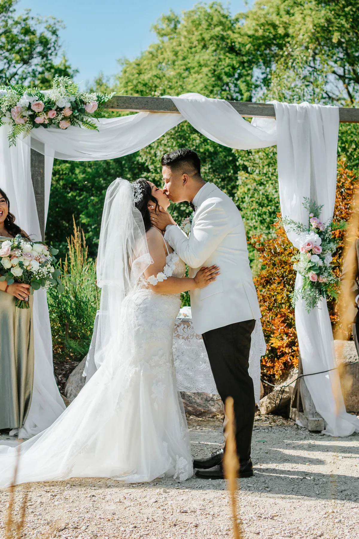 Jay and Mark's first kiss as married couple under the floral arbor at Hawthorne Estates, Manitoba
