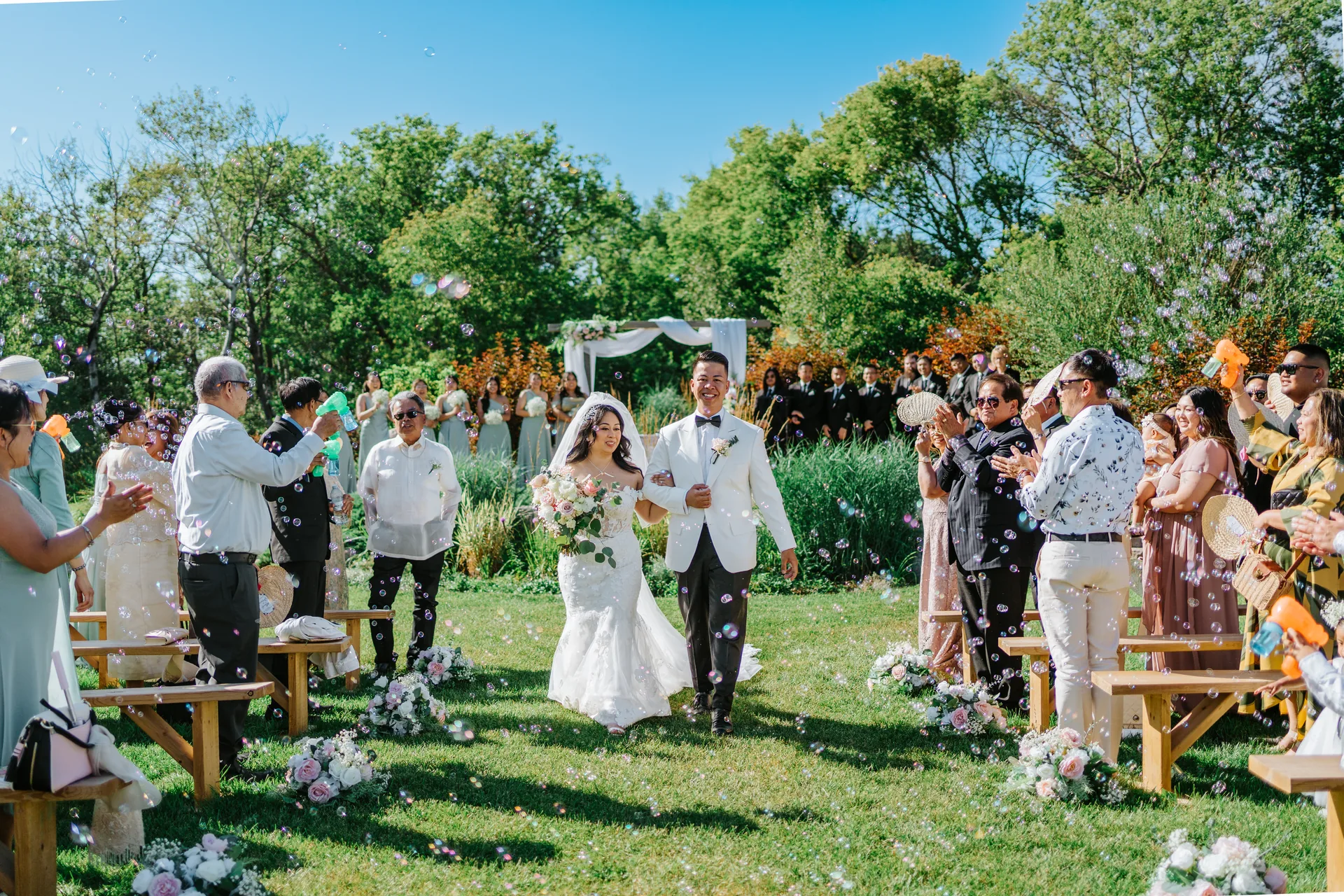 Jay and Mark walking the recessional aisle with guests blowing bubbles at Hawthorne Estates, Manitoba — photographed by Chris Ngo, Ngo Photography