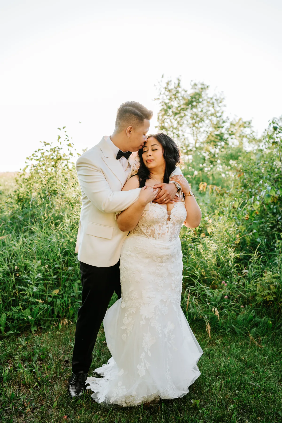 Jay and Mark embracing in dappled golden hour light among trees at Hawthorne Estates, Manitoba