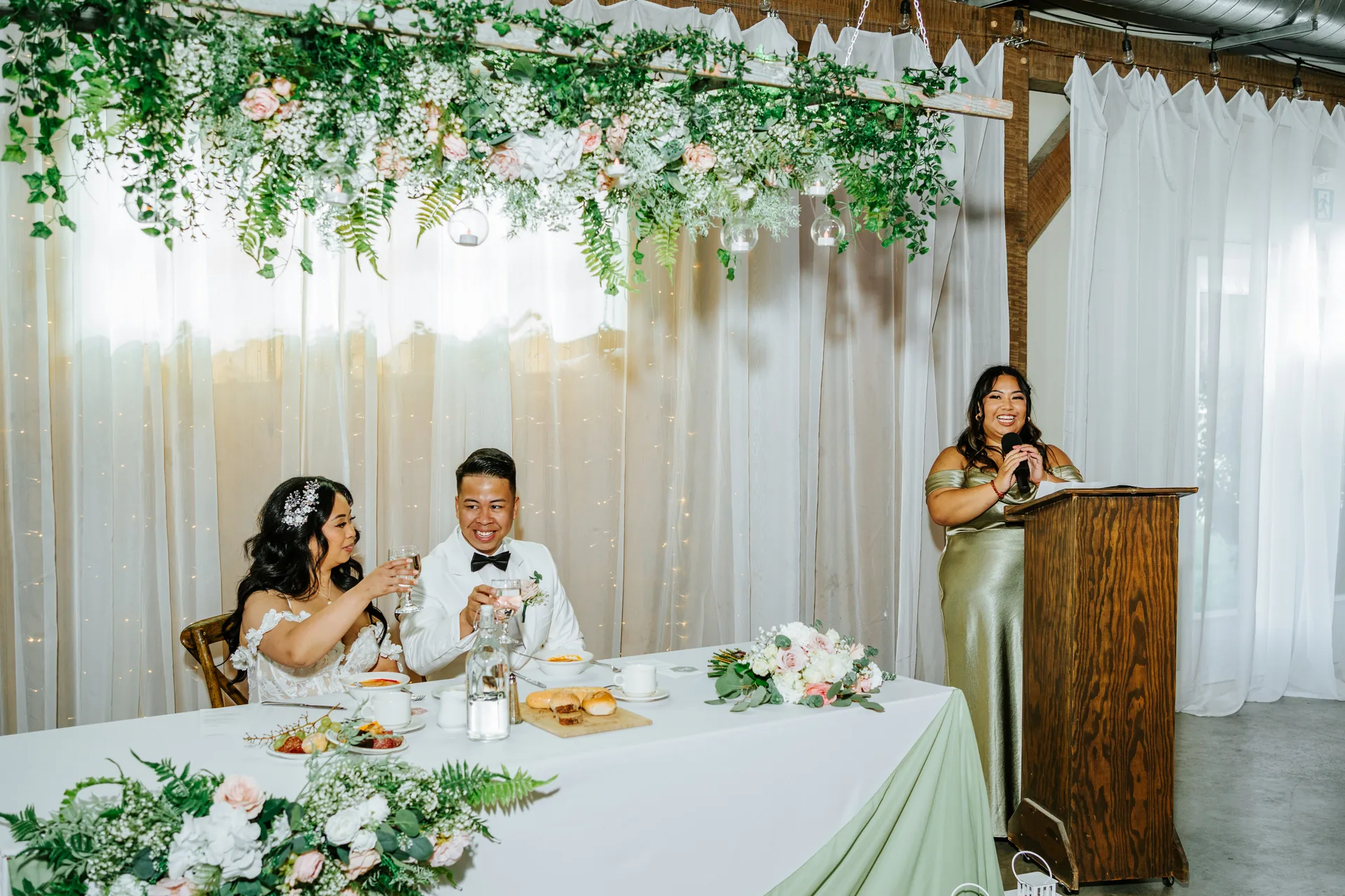 Sweetheart table under lush hanging greenery and florals at Hawthorne Estates reception barn, Manitoba