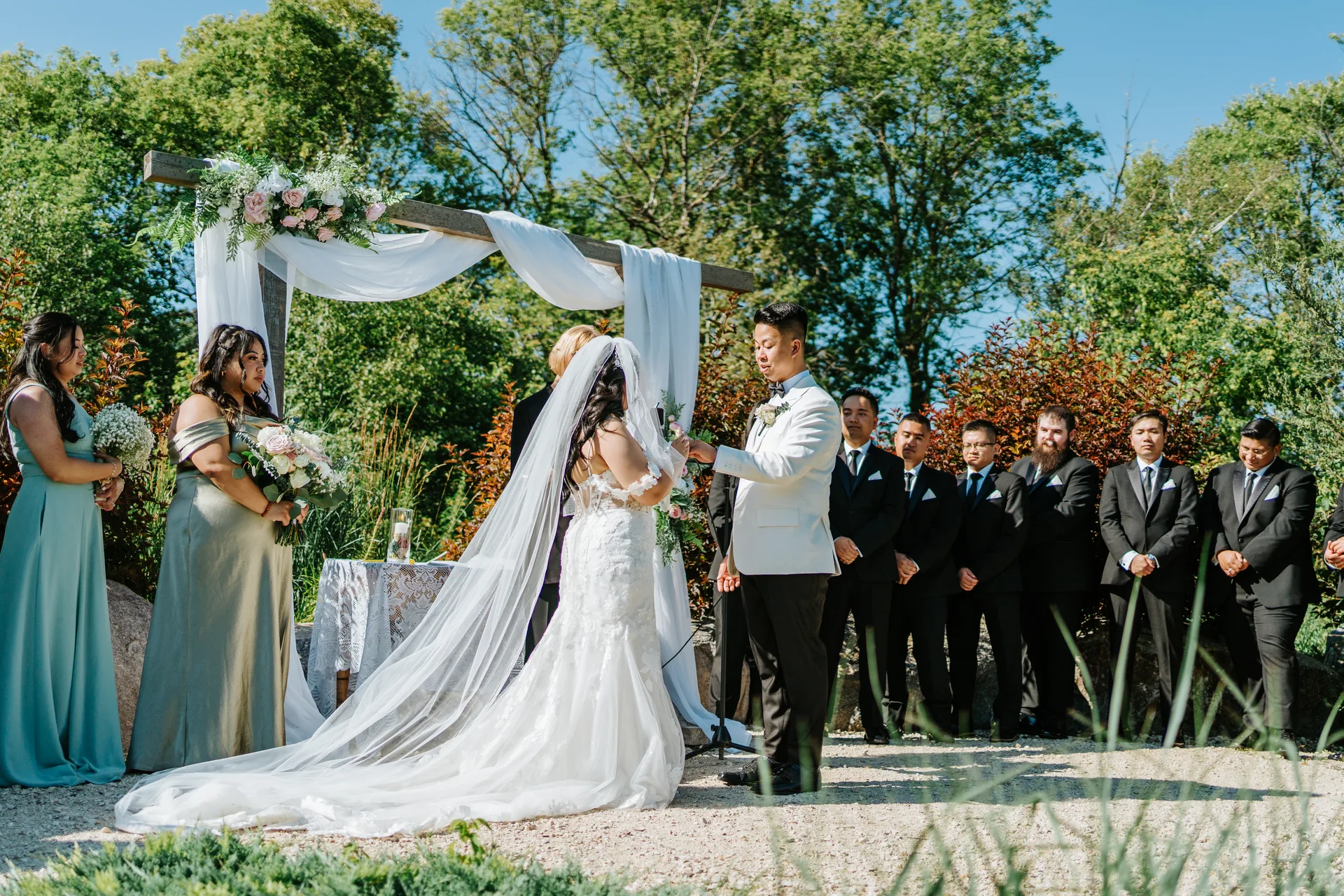 Mark lifting Jay's veil and exchanging rings under the floral arbor at Hawthorne Estates, Manitoba