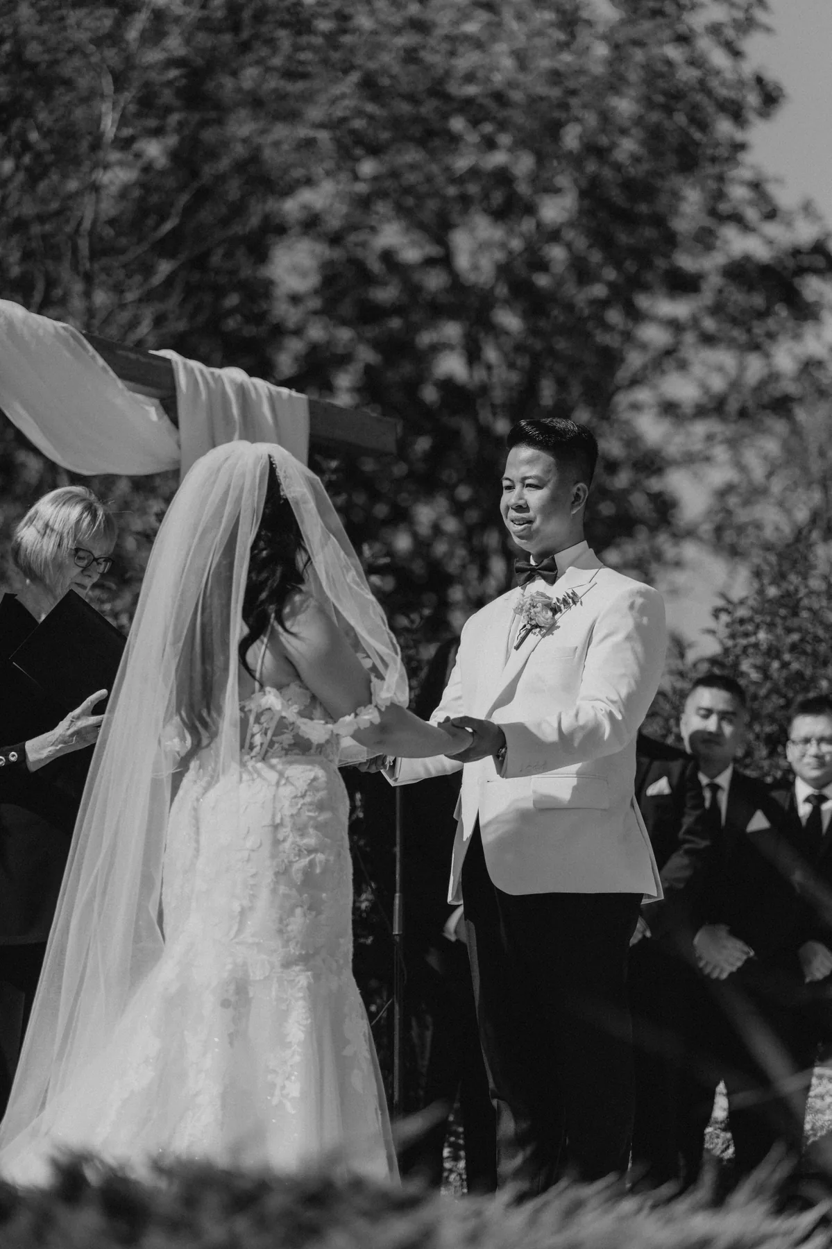 Jay and Mark exchanging vows under the wooden arbor at Hawthorne Estates — black and white, Manitoba