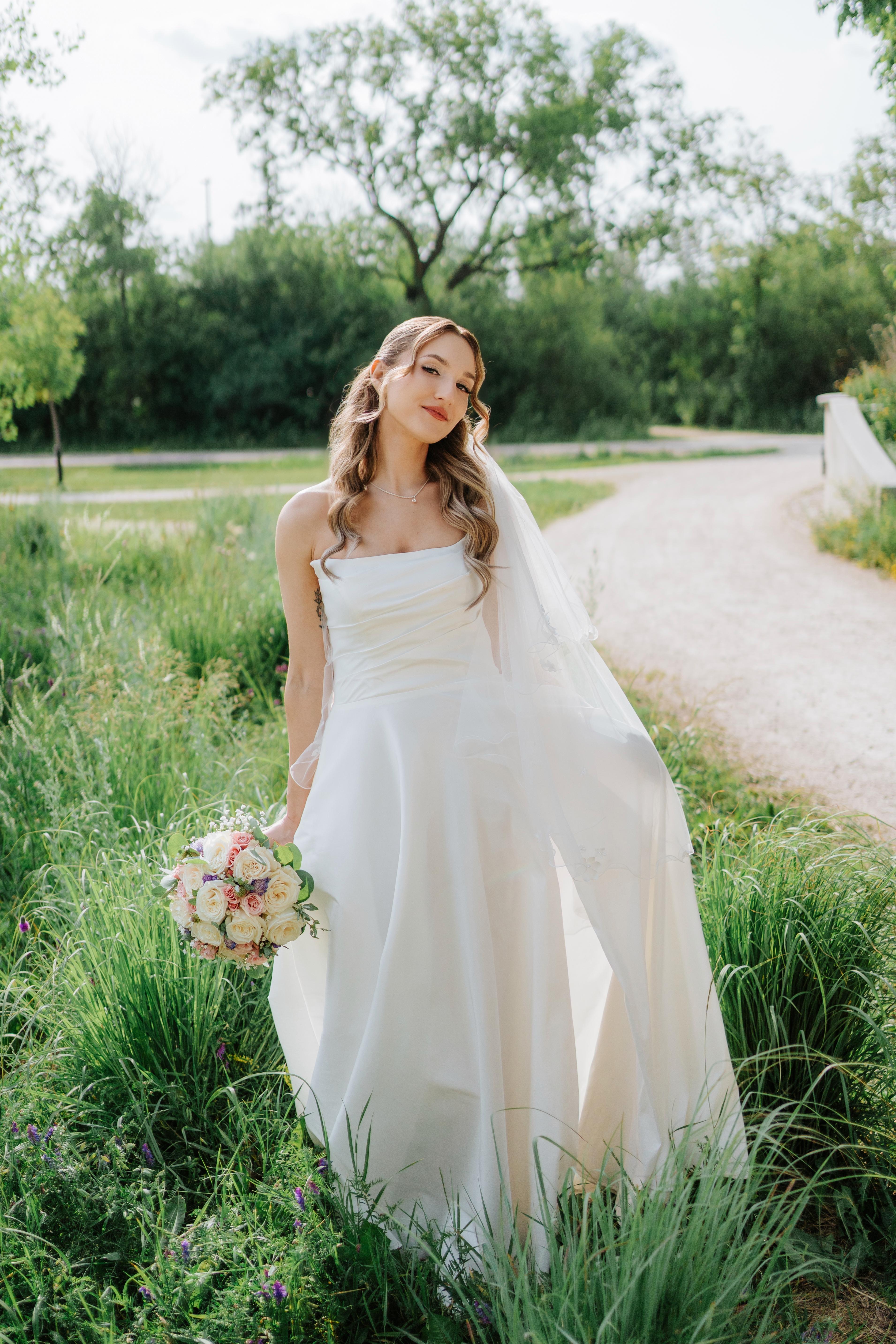 Tanya bridal portrait in white gown and veil standing in a park meadow at Assiniboine Park, looking away — Winnipeg wedding photography by Ngo Photography