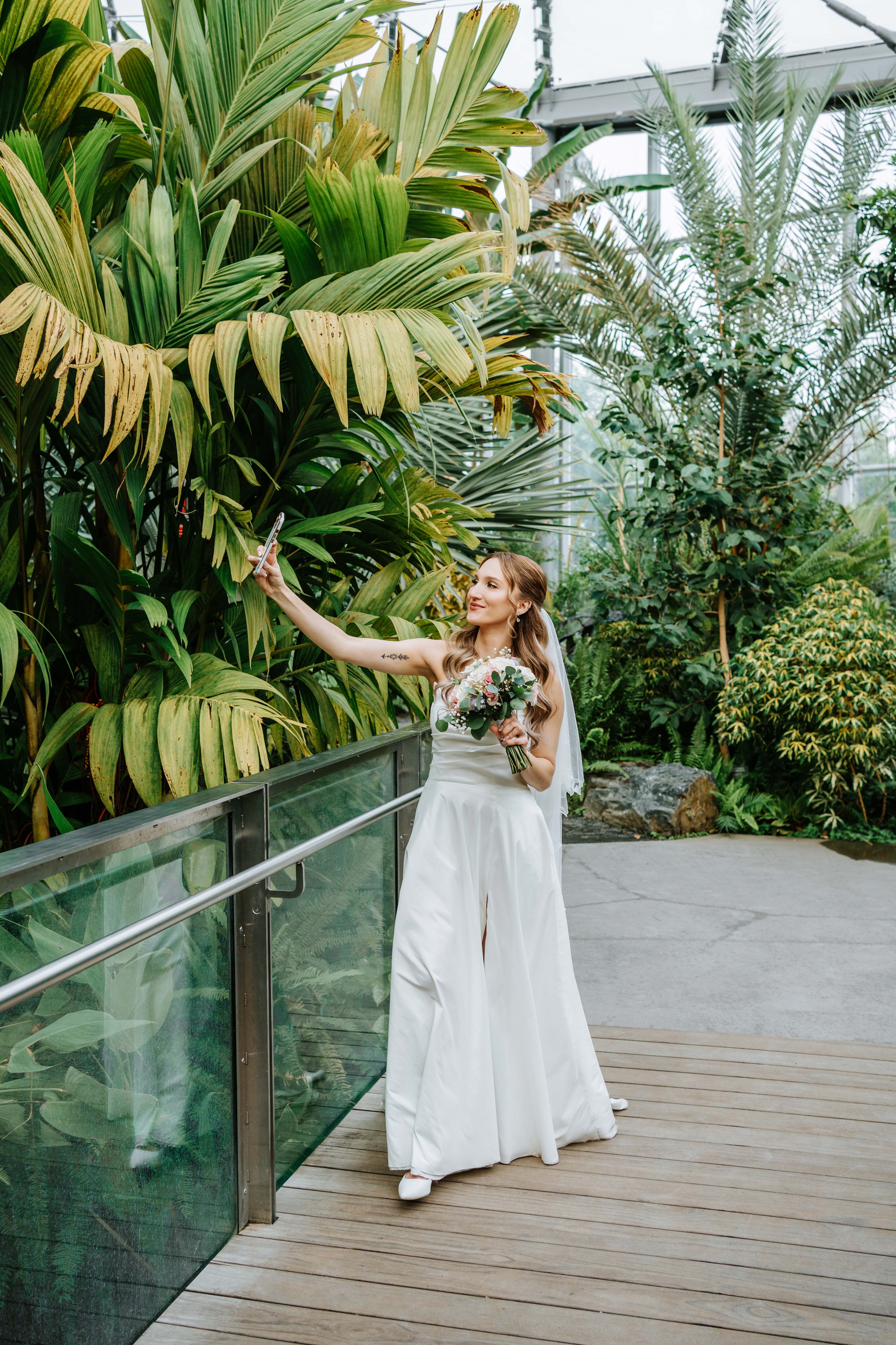 Tanya taking a selfie in front of tropical palm trees inside The Leaf Assiniboine Park botanical garden — fun candid wedding photography by Ngo Photography