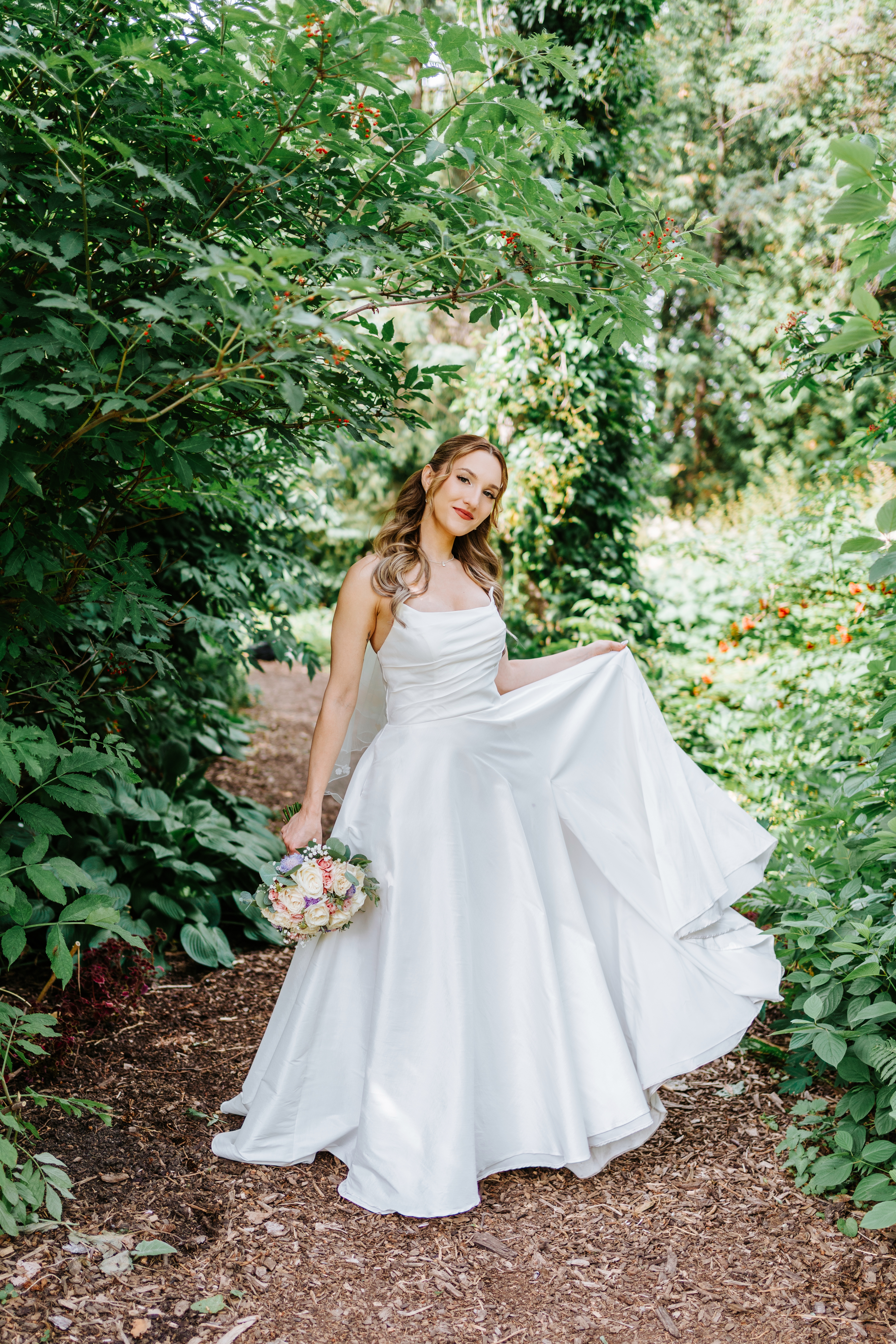 Tanya twirling in her white strapless wedding gown on a lush garden path at Assiniboine Park — wedding photography by Chris Ngo Winnipeg