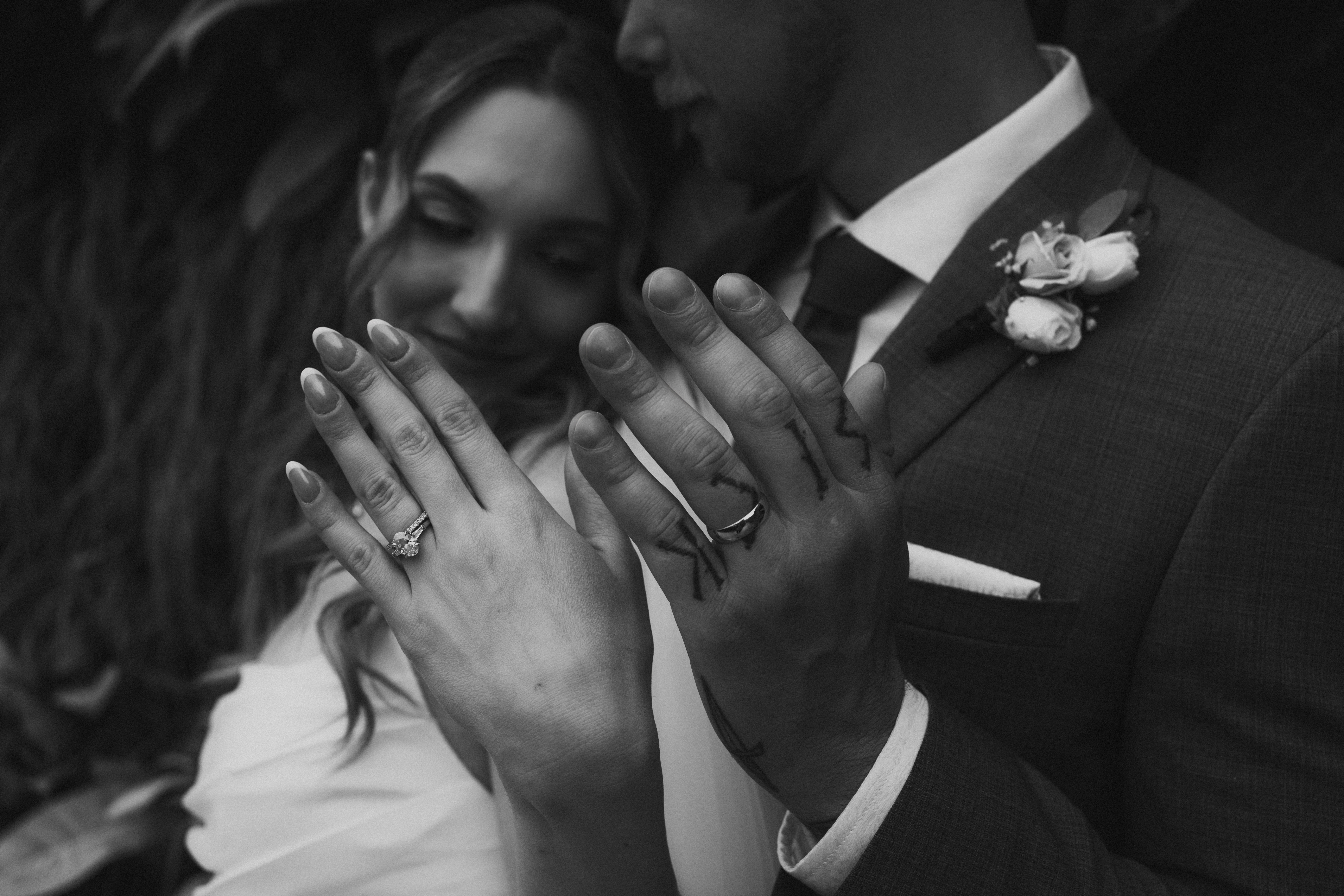 Black and white detail shot of Liam and Tanya's wedding rings on their hands with Liam kissing Tanya's temple — intimate ring detail photography by Ngo Photography Winnipeg