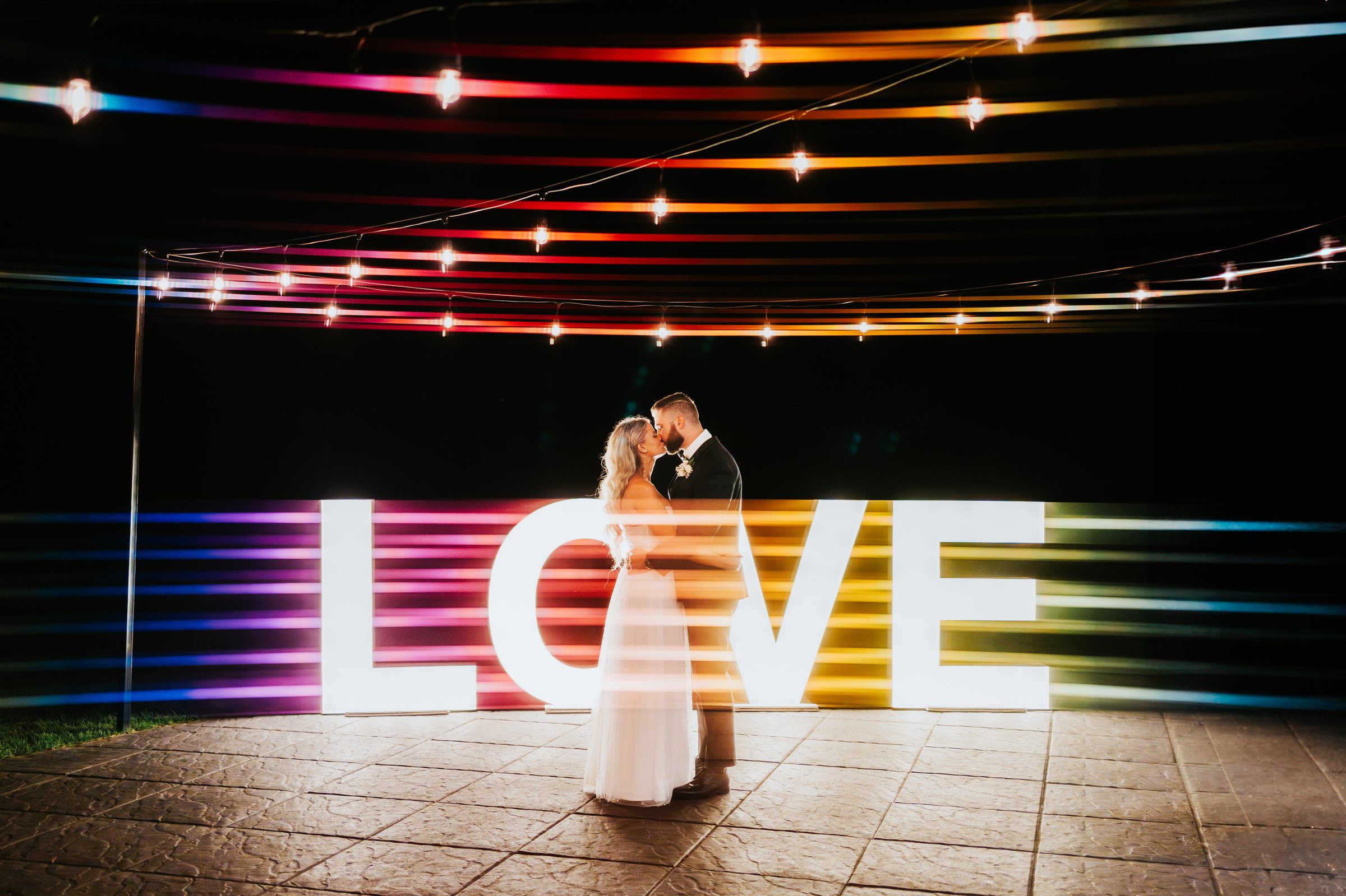 Couple kissing in front of LOVE sign at night — Winnipeg wedding reception photography