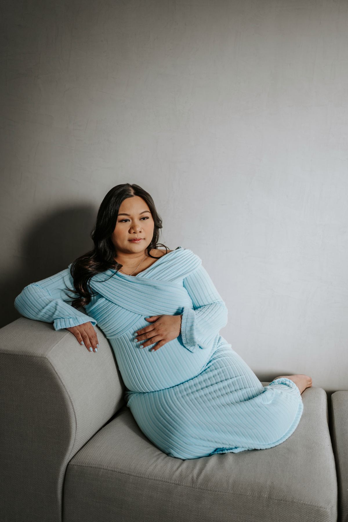 Maternity session in light blue knit dress on studio couch — lifestyle maternity photography Winnipeg by Ngo Photography