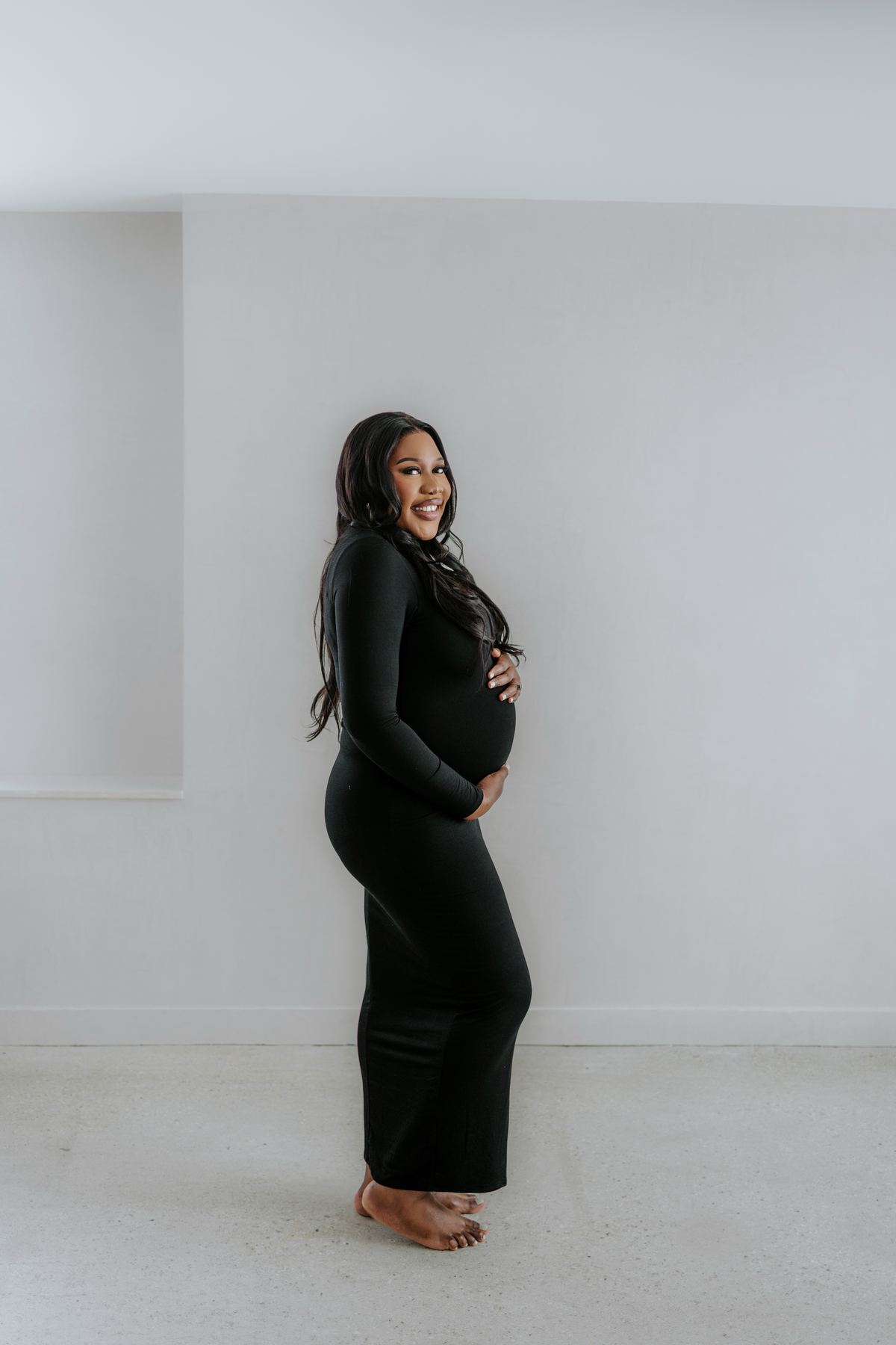 Full-length maternity portrait in black dress against clean white backdrop — Winnipeg studio photography by Ngo Photography