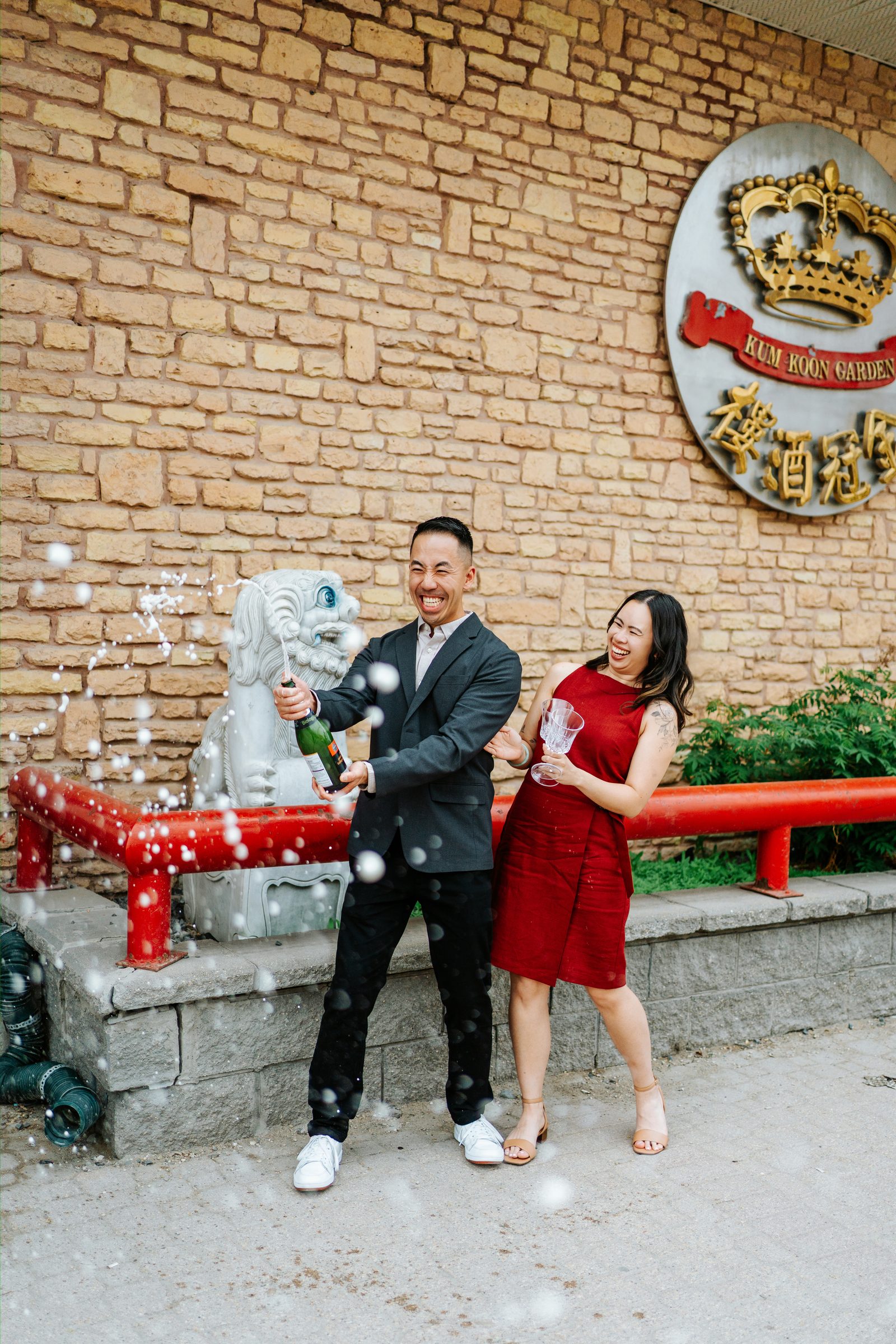 Monica and Jason outside Kum Koon Garden Winnipeg with carved stone lion guardian — Chinese engagement photography by Chris Ngo