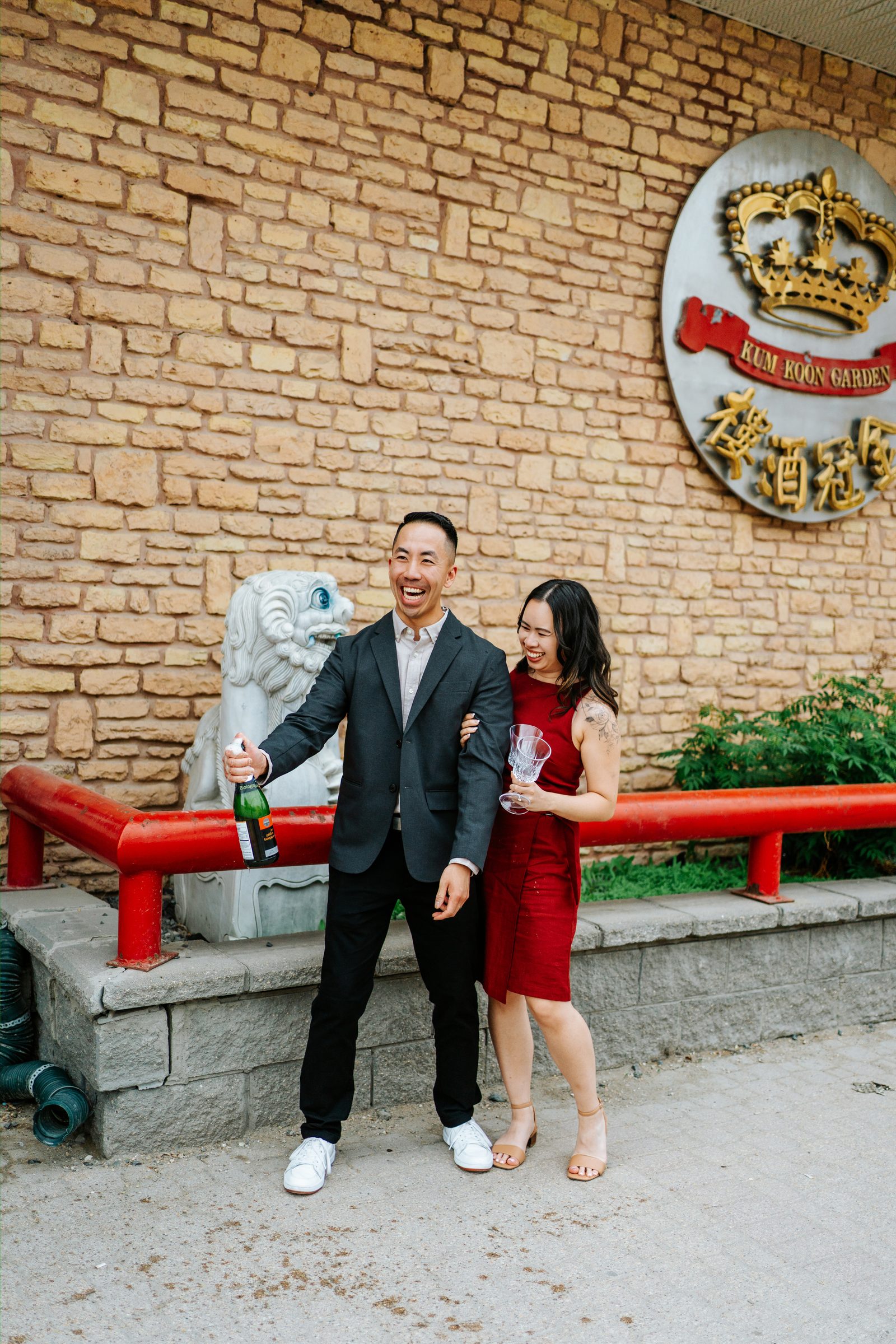 Monica and Jason champagne celebration outside Kum Koon Garden Winnipeg with the iconic crown and Chinese characters sign — engagement photography by Chris Ngo