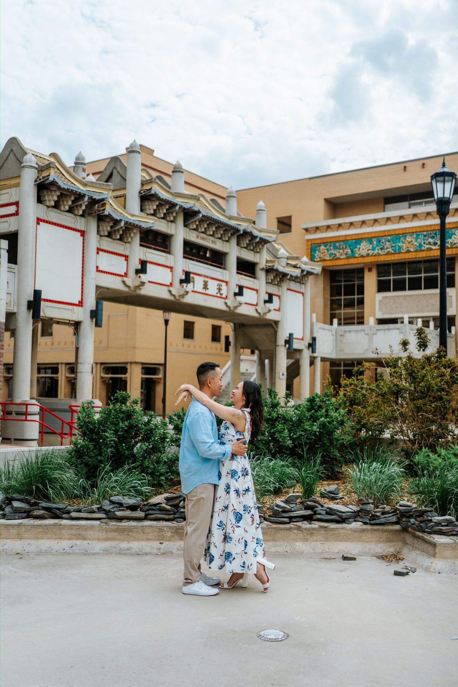 Monica and Jason on the red staircase in Winnipeg Chinatown with green pagoda roof overhead — engagement photography by Chris Ngo