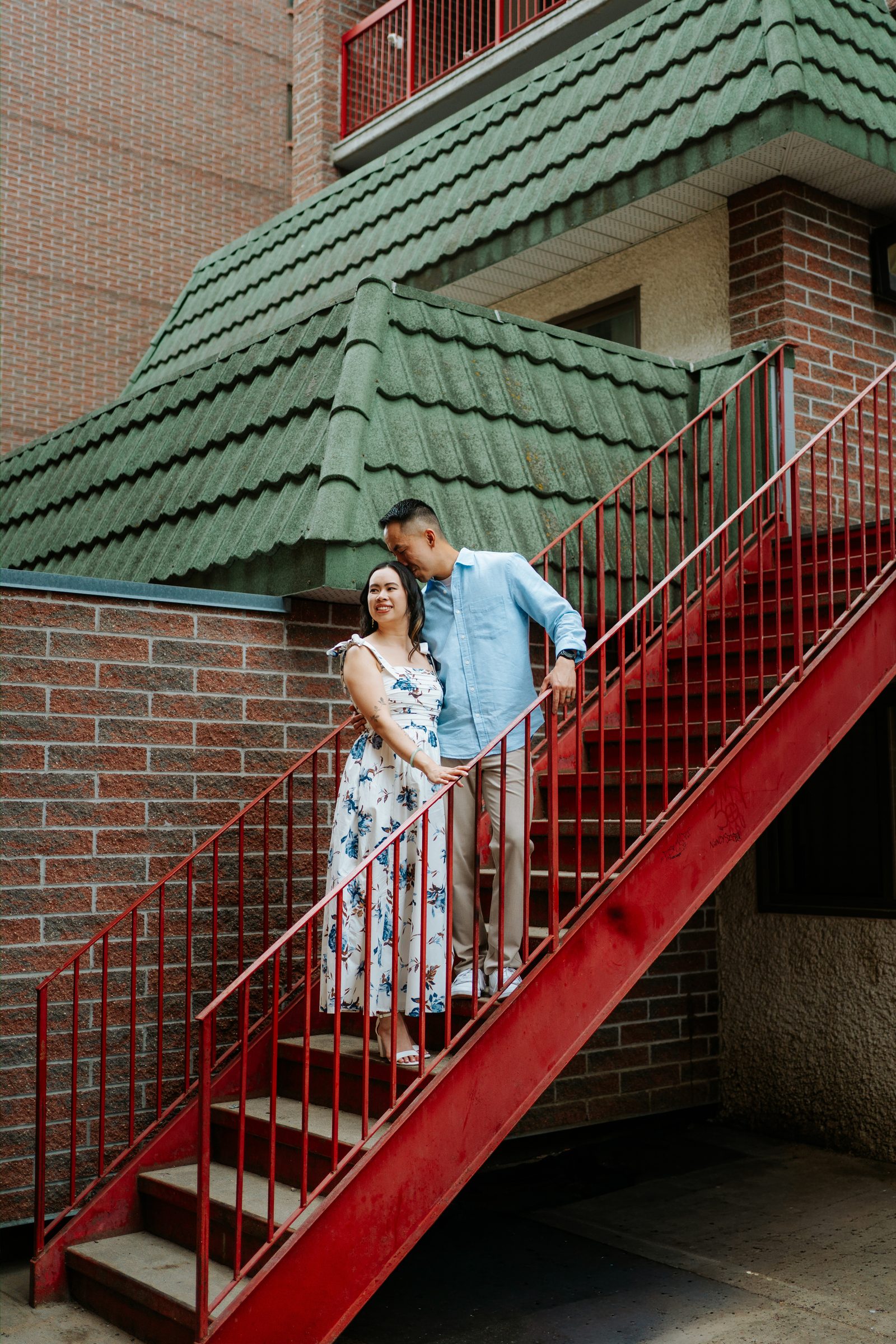 Monica and Jason on the red staircase with green Chinese pagoda architectural detail in Winnipeg Chinatown — engagement photography by Chris Ngo
