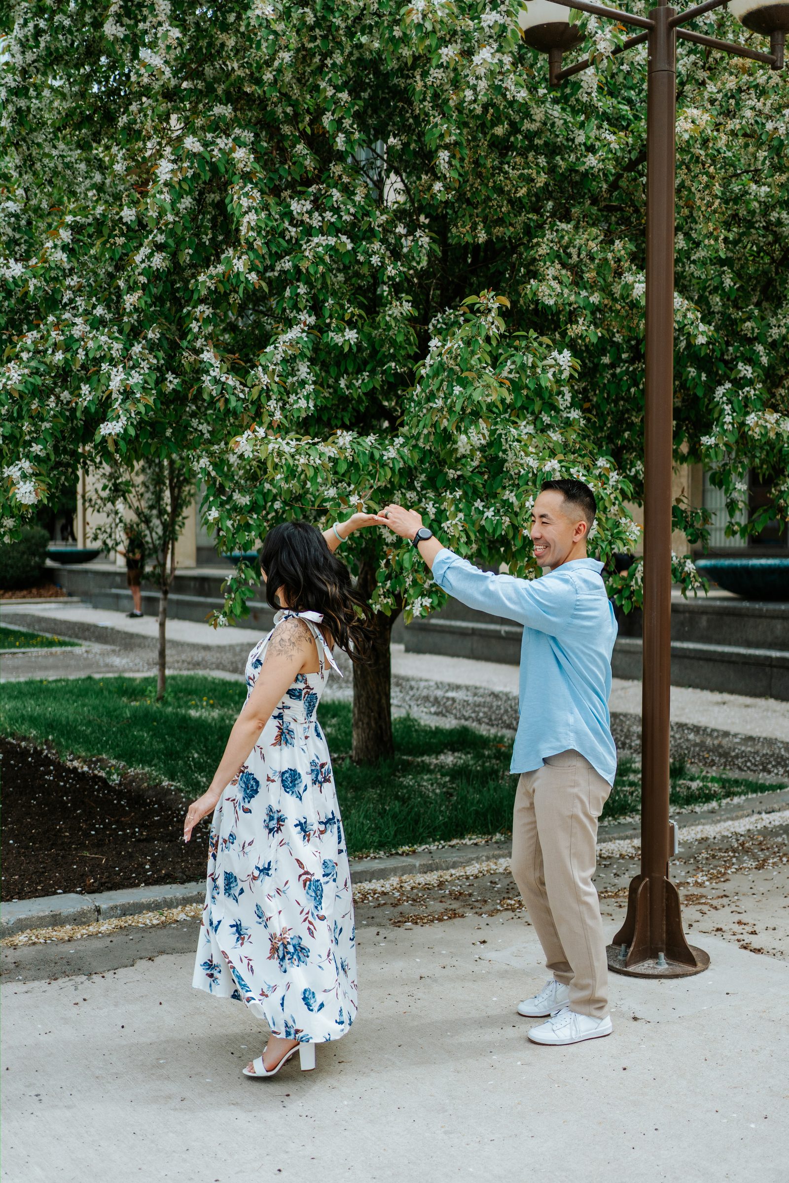 Jason spinning Monica under white blossoming trees in Winnipeg Chinatown — engagement photography by Ngo Photography