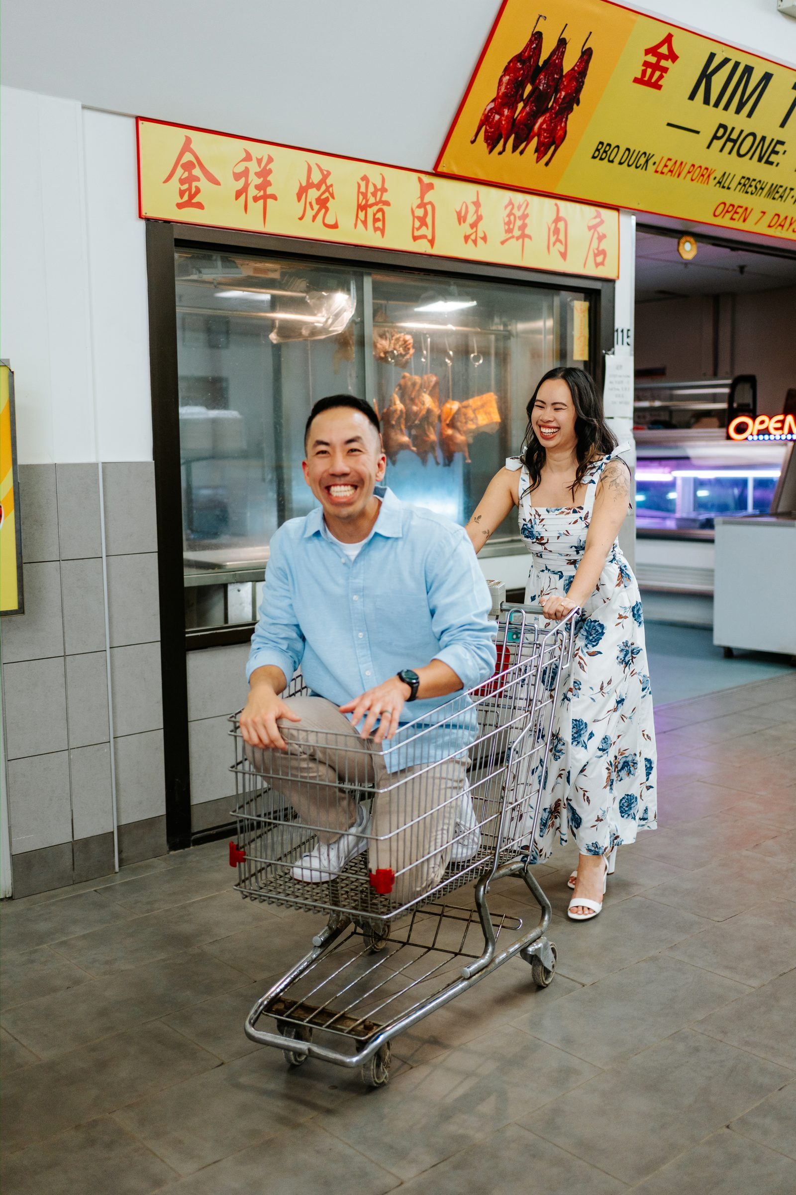 Monica pushing Jason in a shopping cart past Kim Tuong BBQ at Sun-Wah Centre Chinatown Winnipeg — engagement photography by Ngo Photography