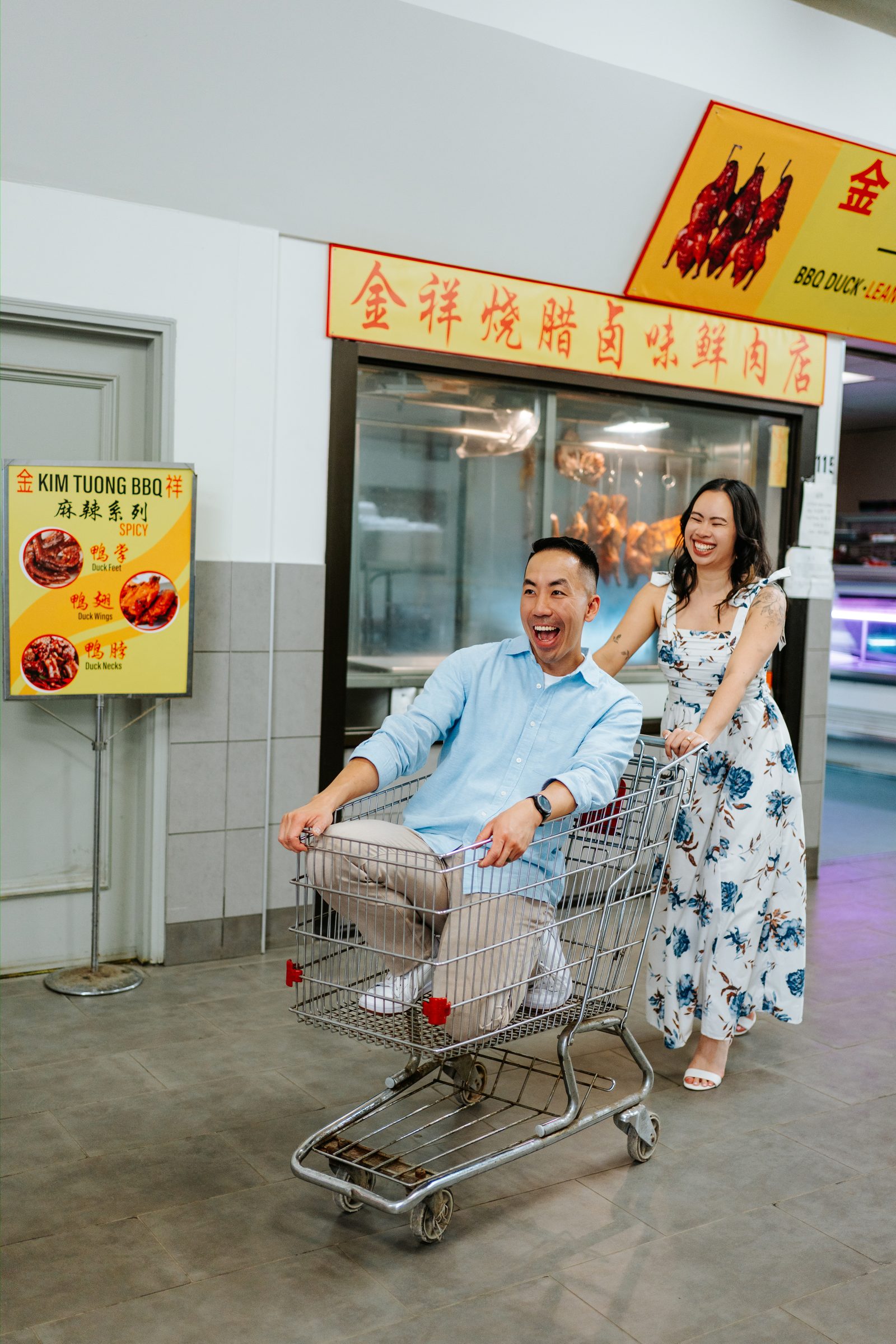 Monica and Jason walking through Sun-Wah Centre with bilingual signs in English Chinese and Vietnamese overhead — Winnipeg Asian grocery engagement photography by Ngo Photography