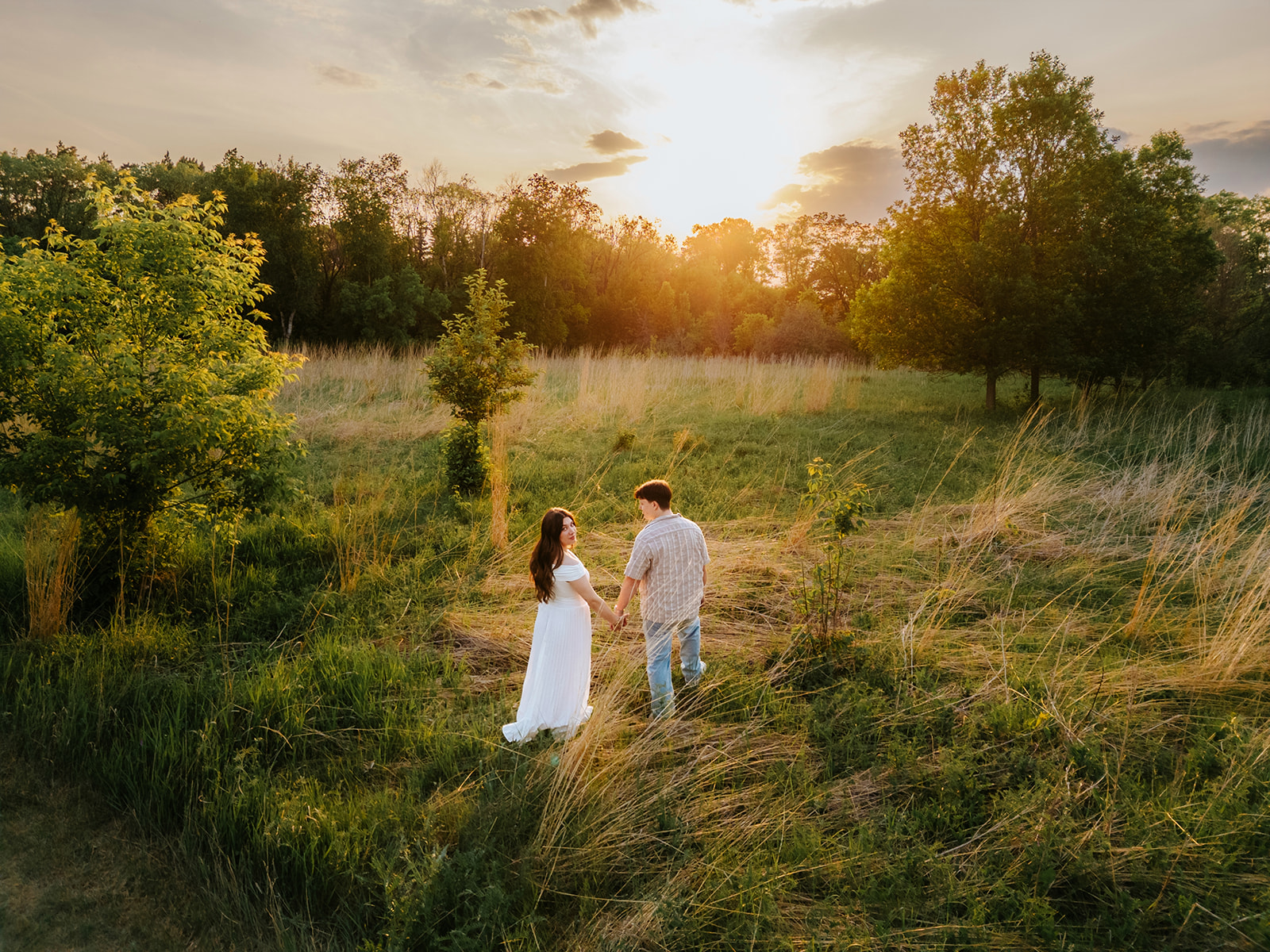 Aerial drone photo of Nick and Kiera walking hand-in-hand through an open prairie field at golden hour near Winnipeg — engagement photography by Ngo Photography