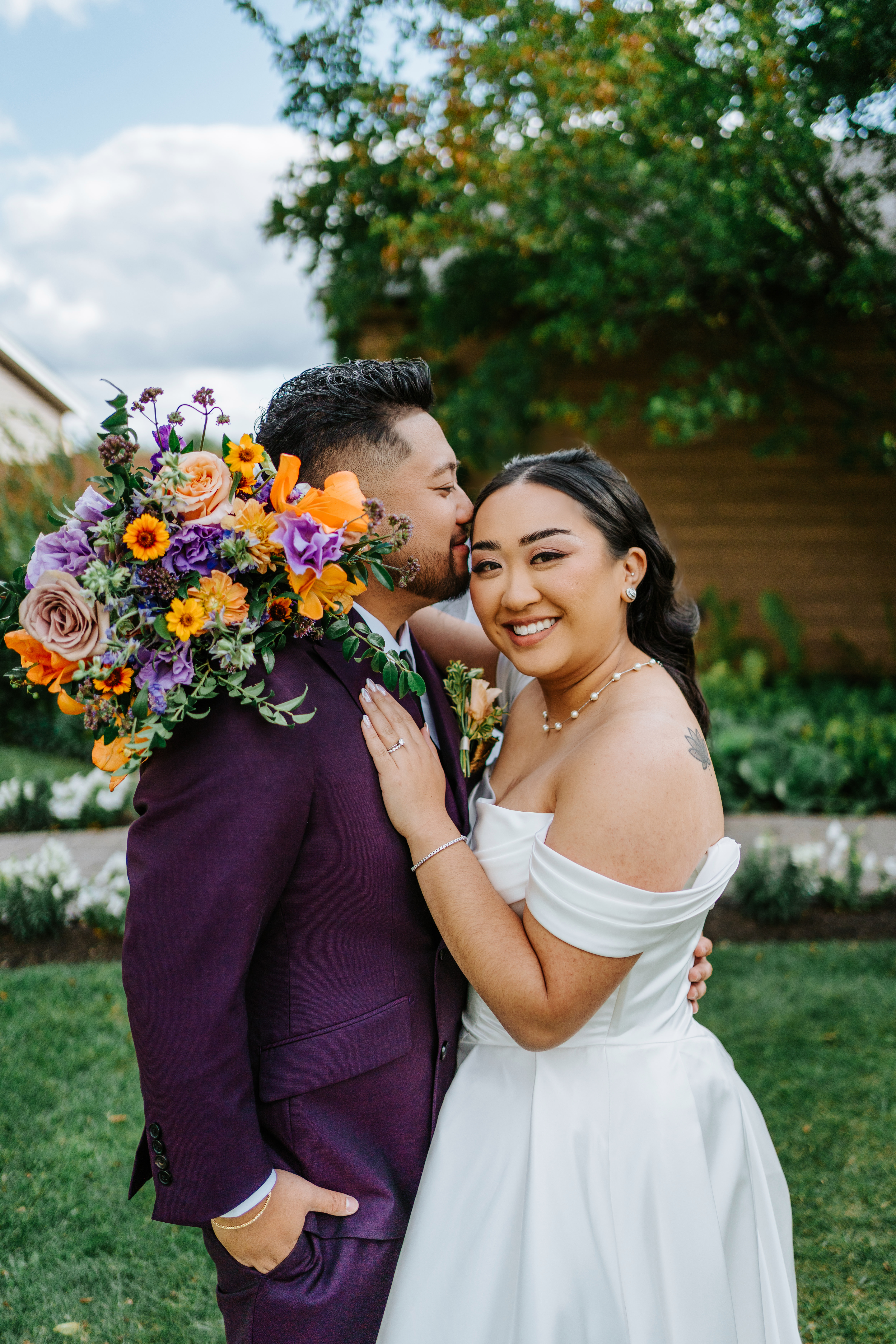Paul and Ayanna together in the Breezy Bend gardens, Paul in deep plum suit and Ayanna in her off-shoulder ballgown — Ngo Photography Winnipeg