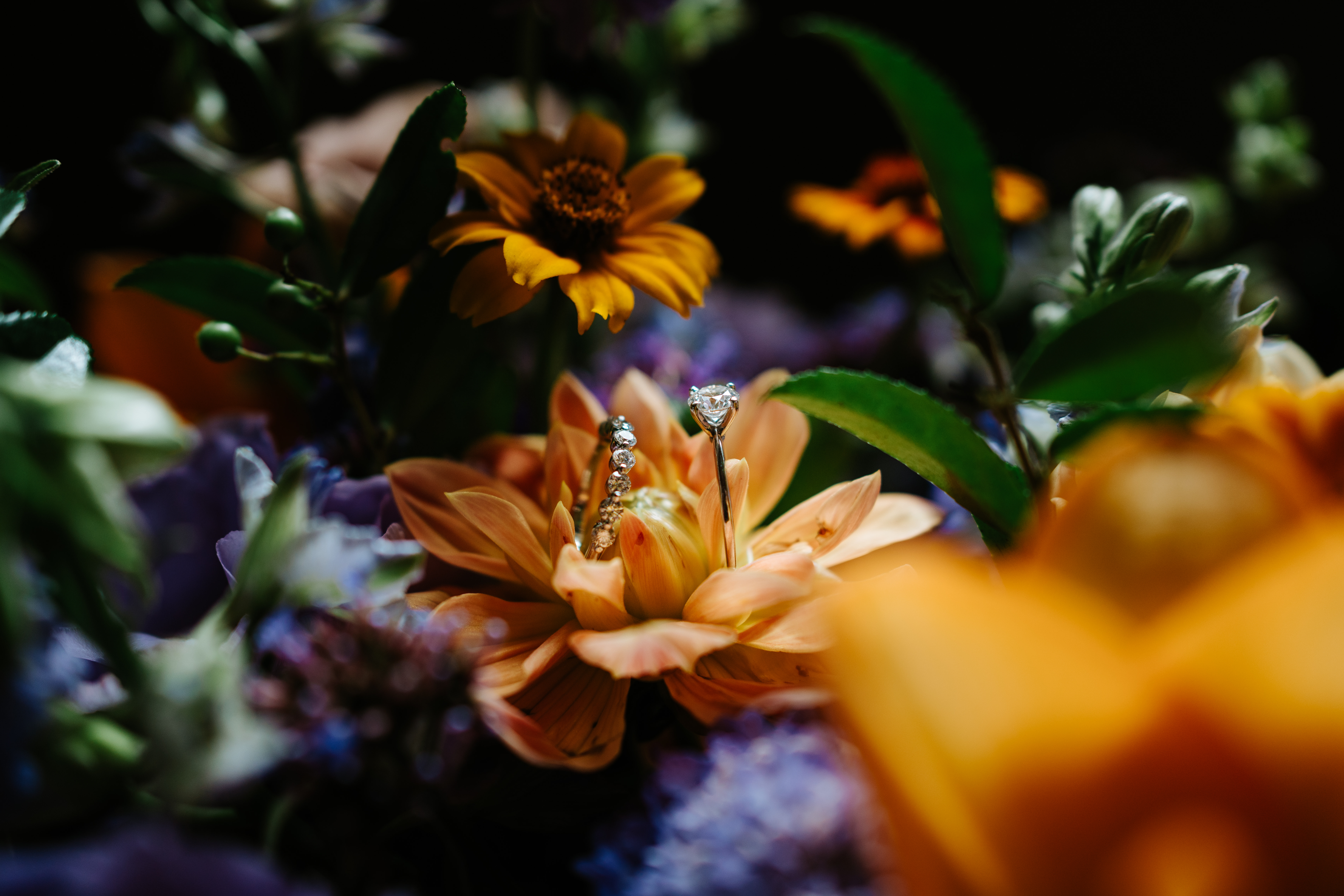 Ayanna's diamond engagement ring nestled in an orange dahlia bloom in the bridal bouquet — Breezy Bend wedding detail photography by Ngo Photography