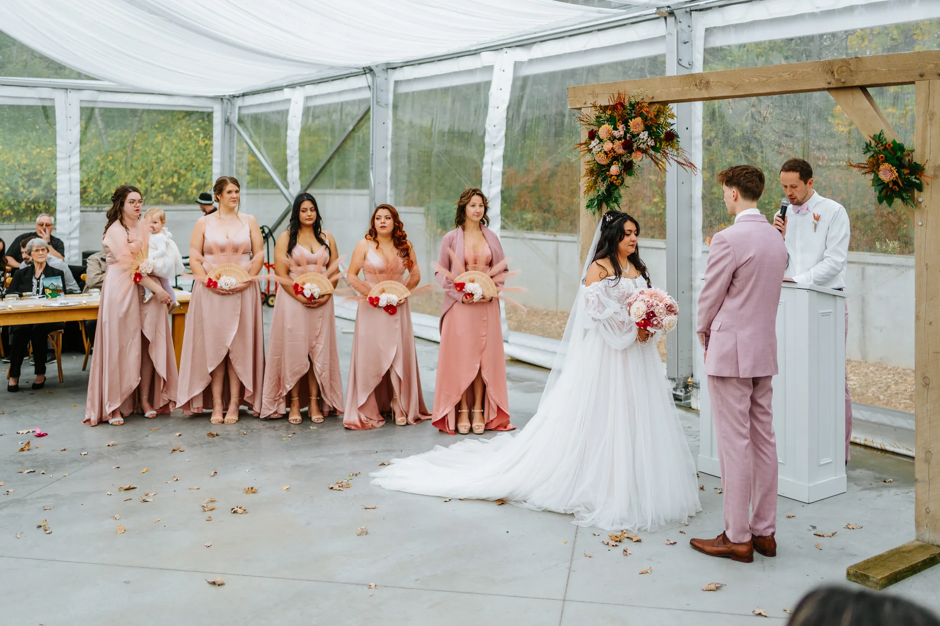 Bride Paola walking the processional aisle in white tulle gown inside the glass tent at Oakland Estates Manitoba wedding