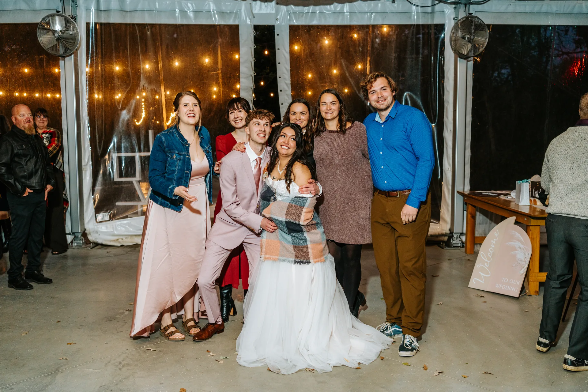 Full wedding group photo under string lights in the glass tent at night — Oakland Estates Manitoba wedding photography