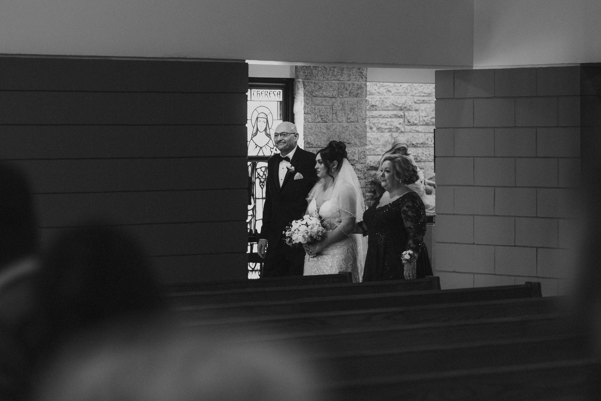 Bride walking the aisle with her parents during the processional at Holy Rosary Church, Winnipeg