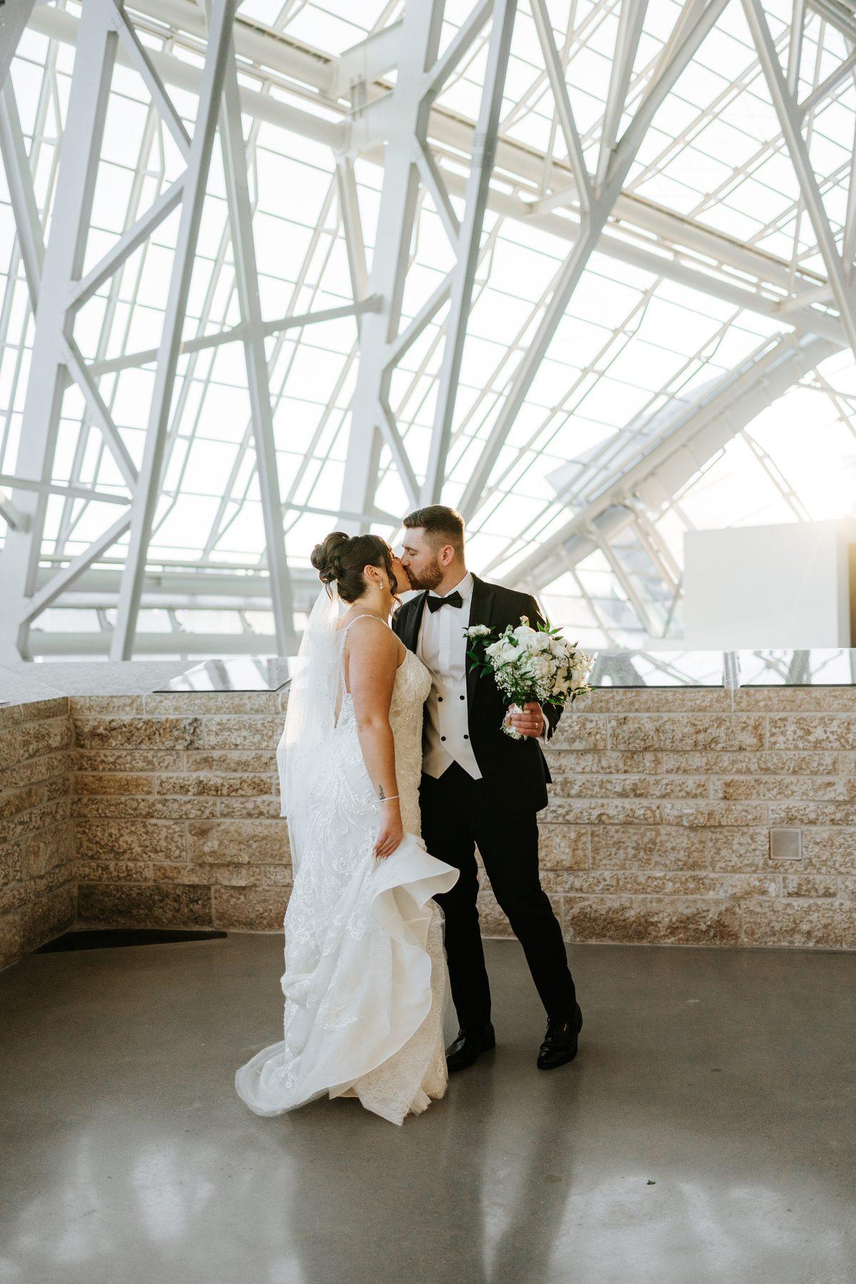 Stef and Brett in a tender moment at the Canadian Museum for Human Rights Winnipeg, the glass tower structure framing them — wedding portrait by Ngo Photography