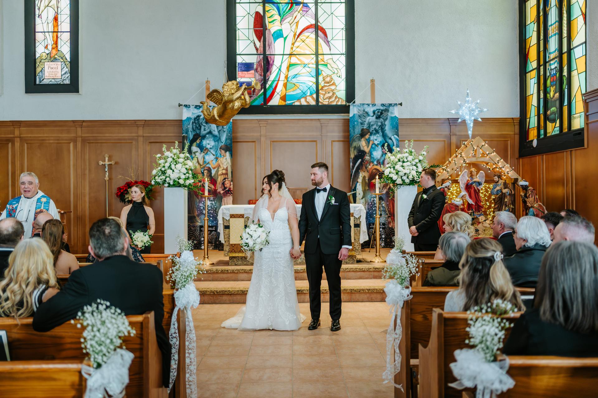 Wide view of Stef and Brett's ceremony at Holy Rosary Church Winnipeg, showing the full nave, congregation, and stained glass altar — wedding photography by Ngo Photography