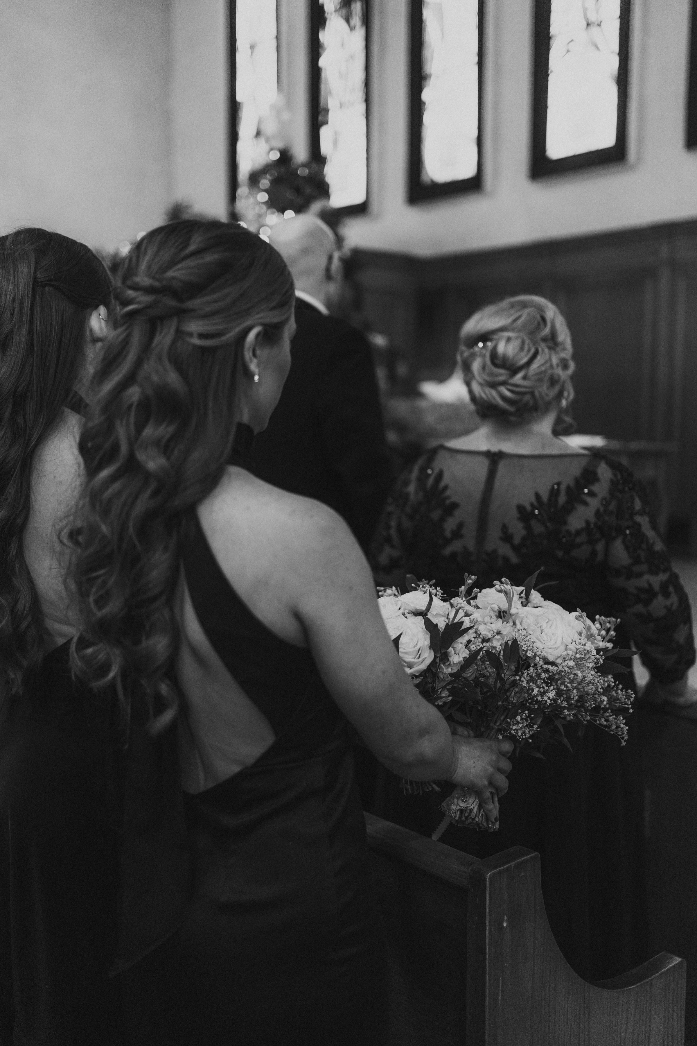 Bridesmaids standing in the church aisle during Stef and Brett's wedding ceremony — black and white wedding photography by Ngo Photography Winnipeg