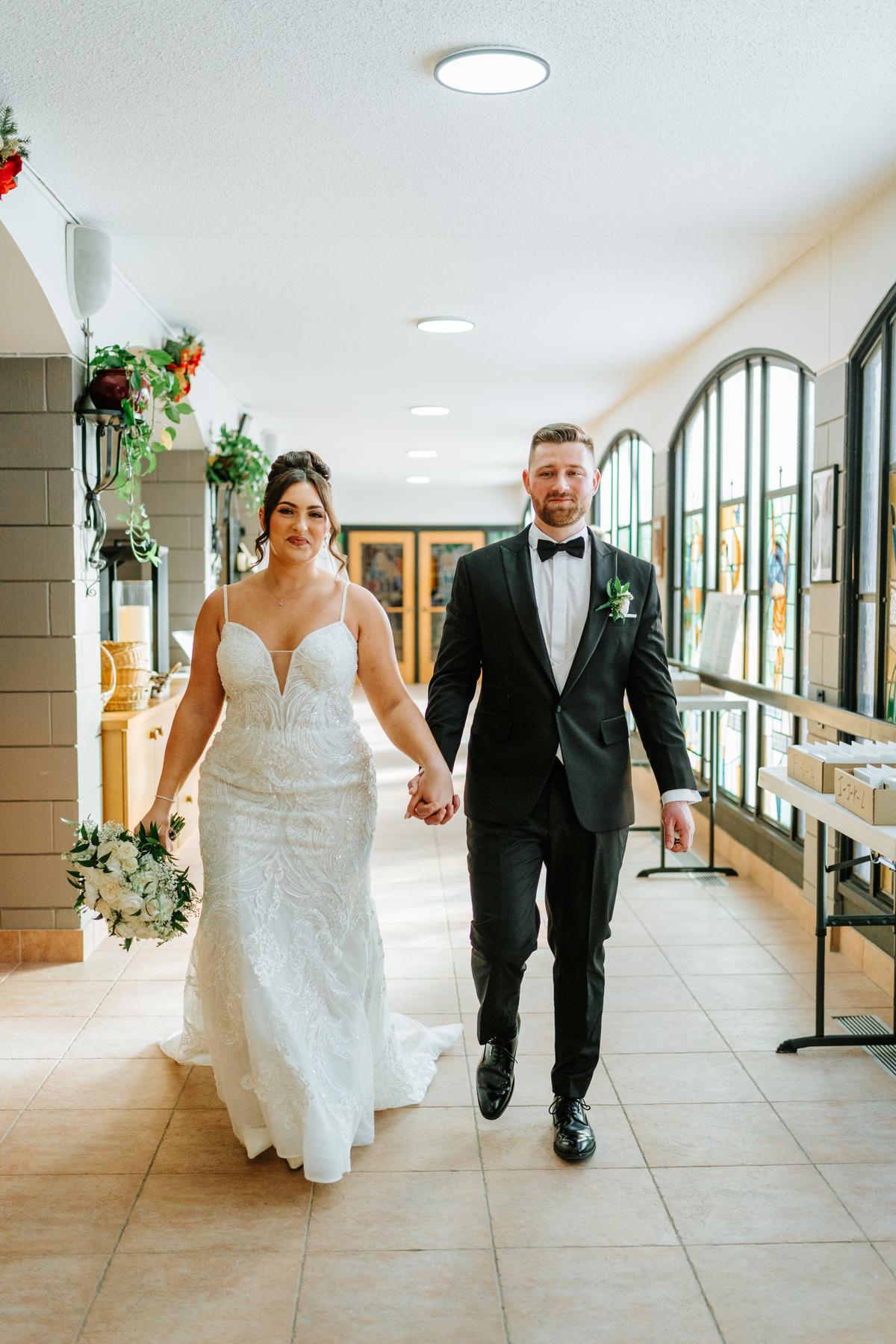 Stef and Brett in the sunlit narthex of Holy Rosary Church Winnipeg, arched windows filling the space with light — post-ceremony wedding portrait by Ngo Photography