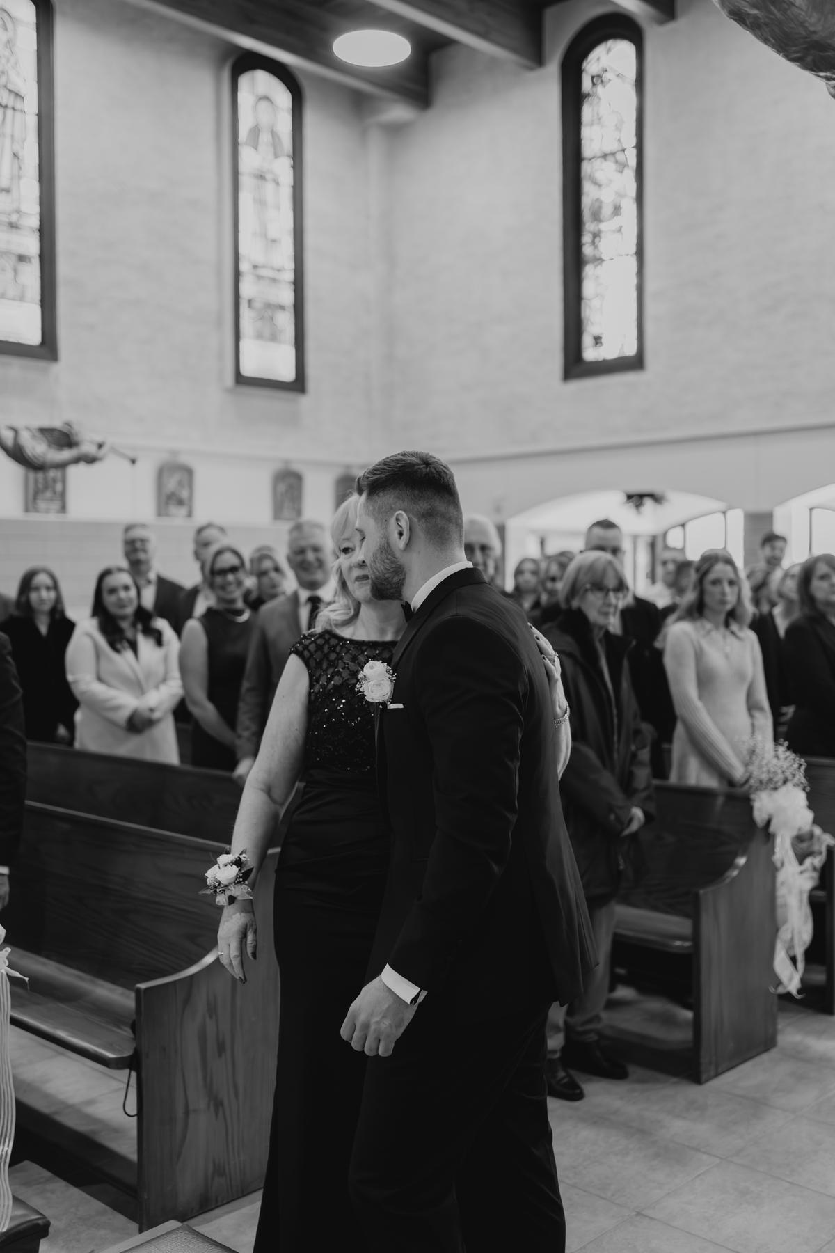 Brett being escorted down the aisle by his mother at Holy Rosary Church Winnipeg — Catholic wedding ceremony photography by Ngo Photography