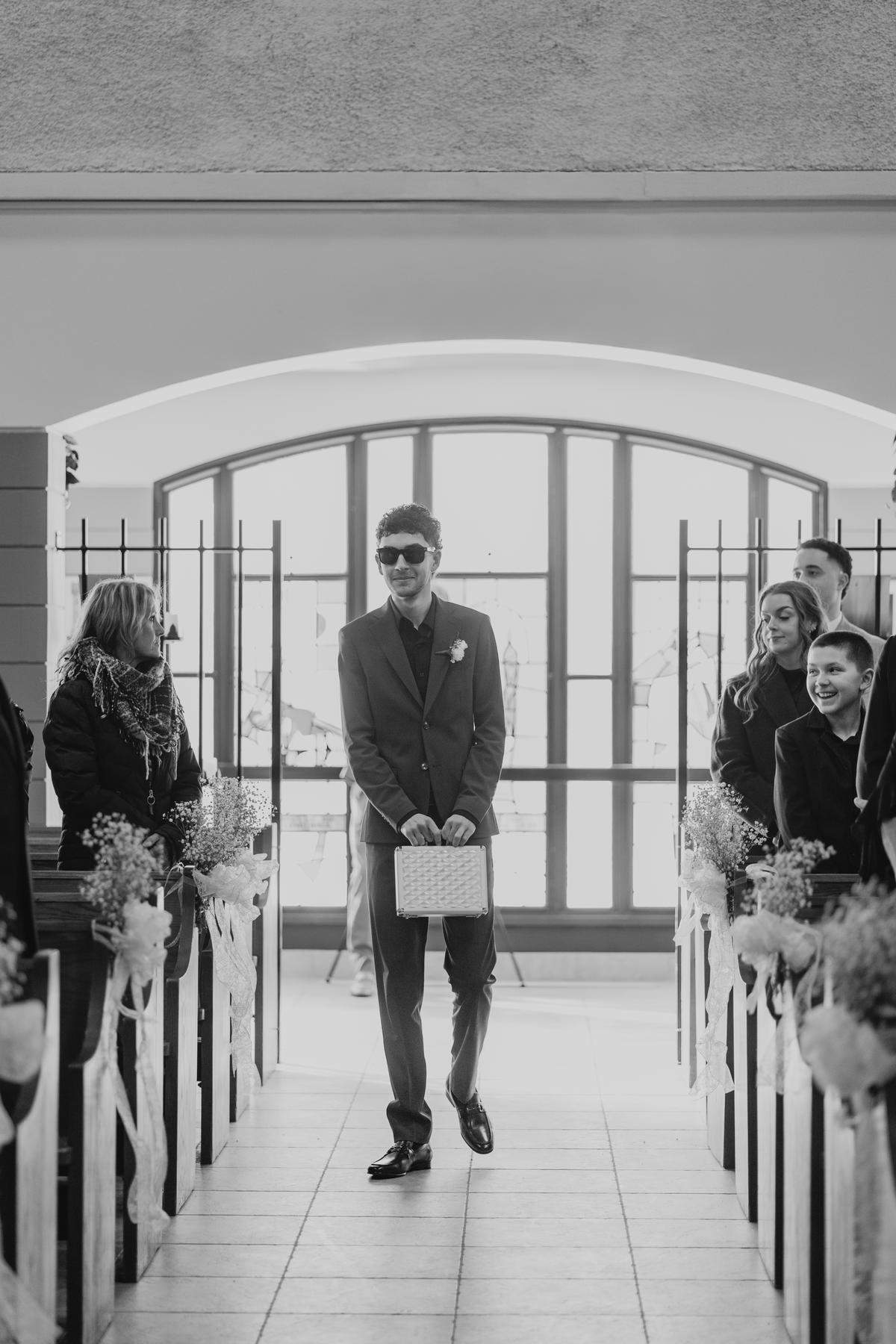 Groomsman walking down the aisle at Holy Rosary Church, the large arched back window behind him — wedding photography by Ngo Photography Winnipeg
