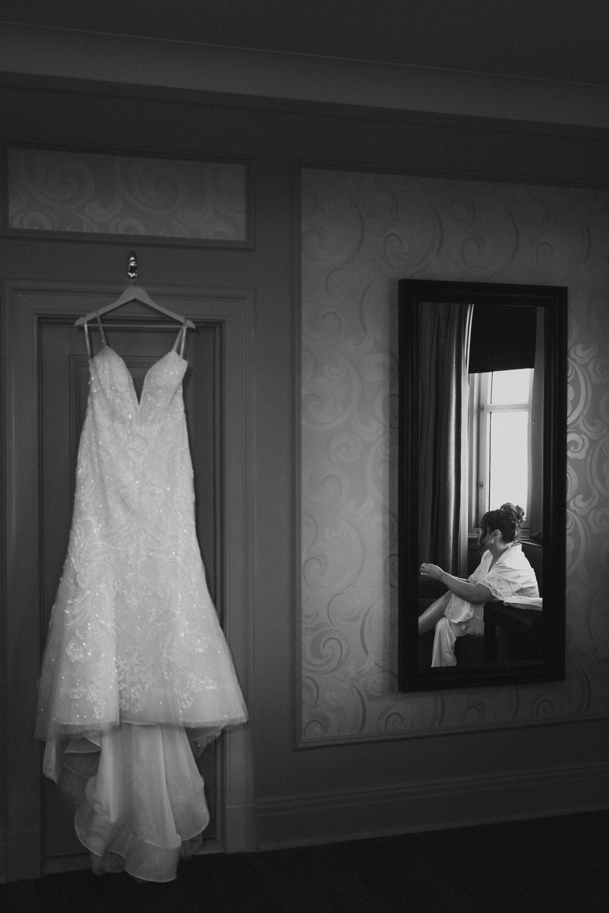 Wedding dress hanging in a tall window at The Fort Garry Hotel with mirror reflection — wedding detail photography by Chris Ngo, Ngo Photography Winnipeg