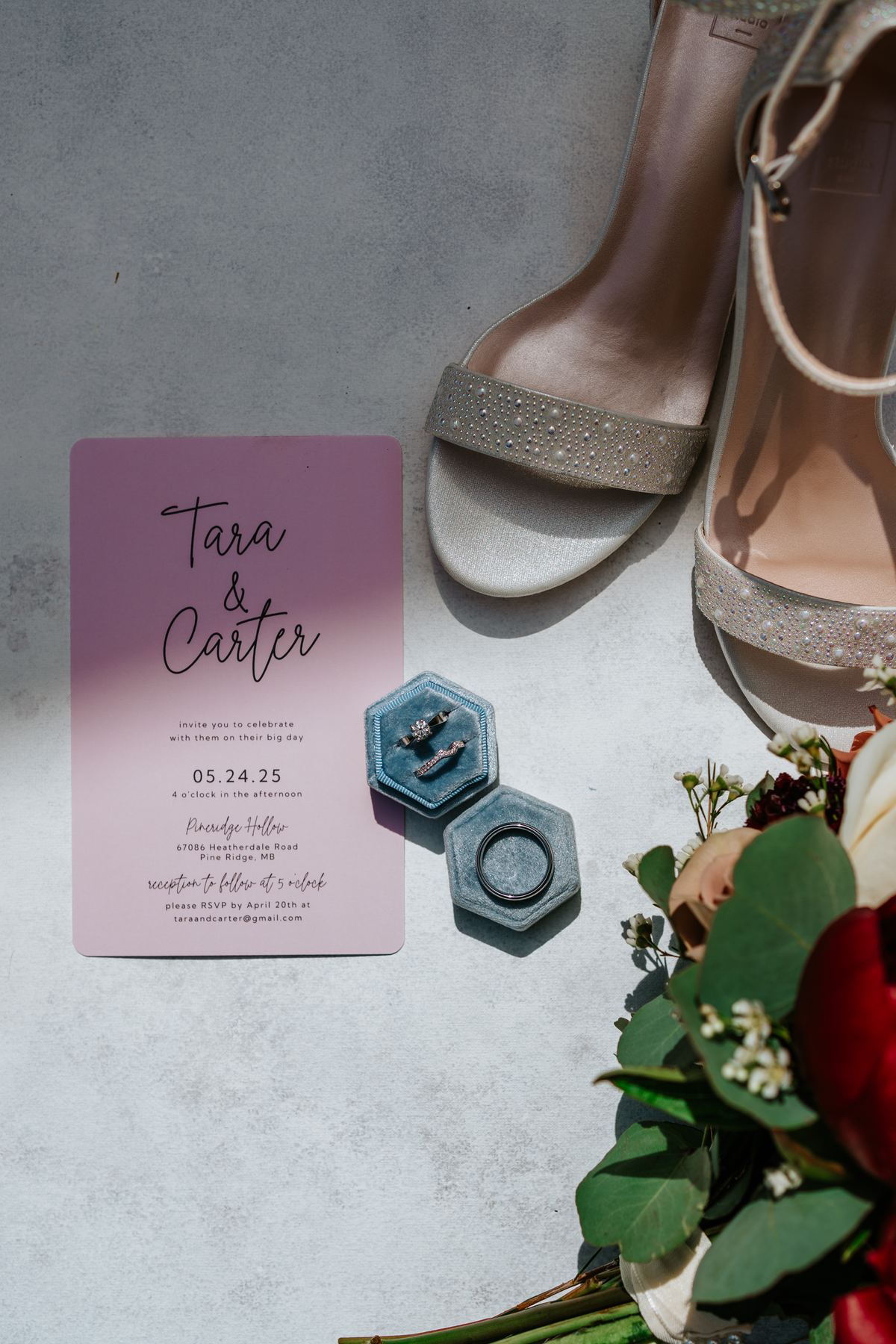 Wedding details flatlay — invitation, rings in blue velvet boxes, and heels for Tara and Carter's Pineridge Hollow wedding, Manitoba