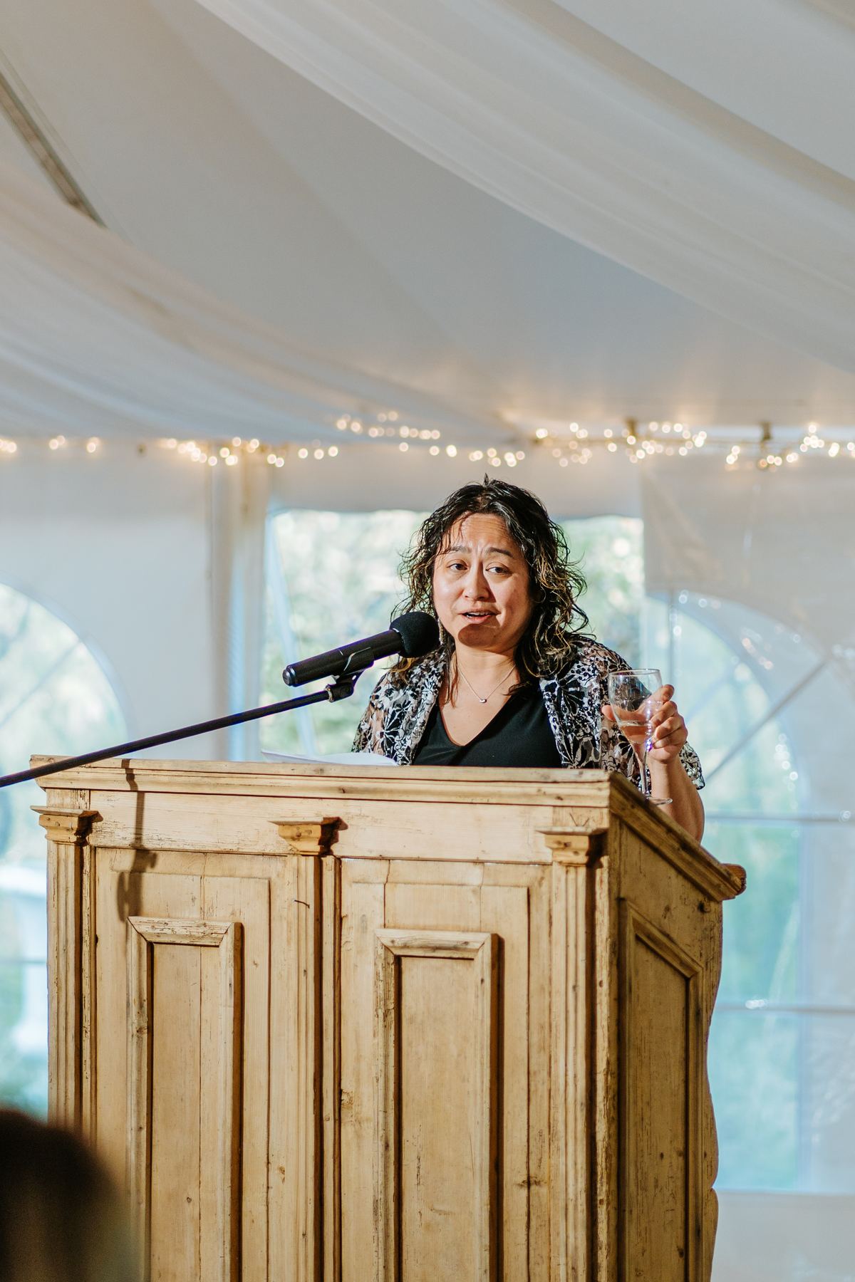 Speech at the podium during Pineridge Hollow wedding reception, string lights in the white canvas pavilion, Manitoba