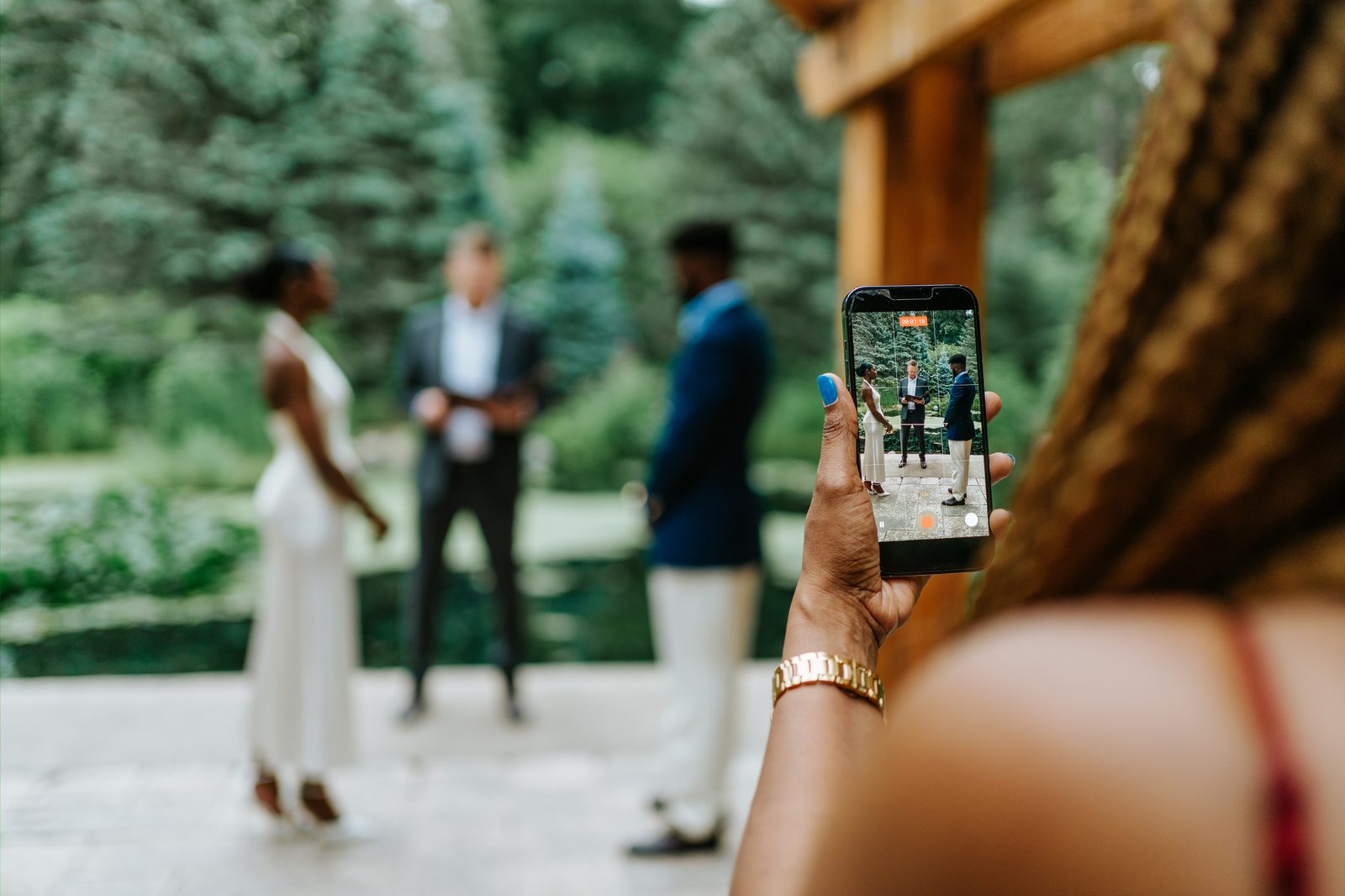 Tobi and Emeka during their ceremony at Leo Mol Sculpture Garden in Assiniboine Park — candid moment, the officiant visible to one side, Winnipeg