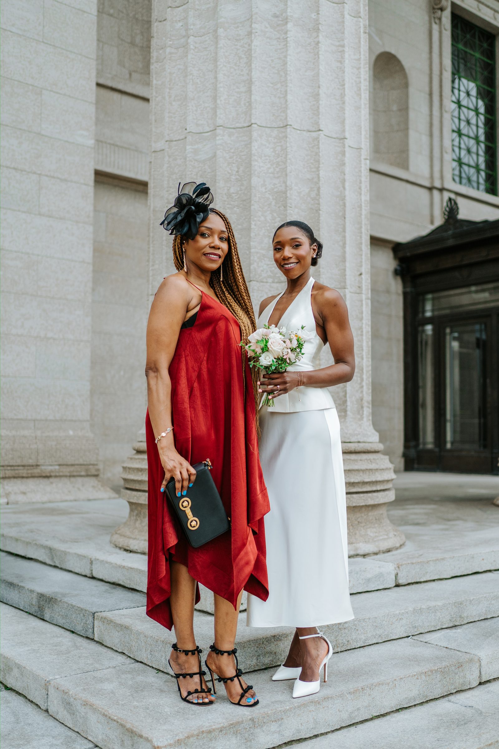 Tobi and a guest — a woman in a flowing red dress with a black fascinator and Versace clutch — on the exterior steps of the Manitoba Legislative Building, Winnipeg — candid family portrait by Ngo Photography