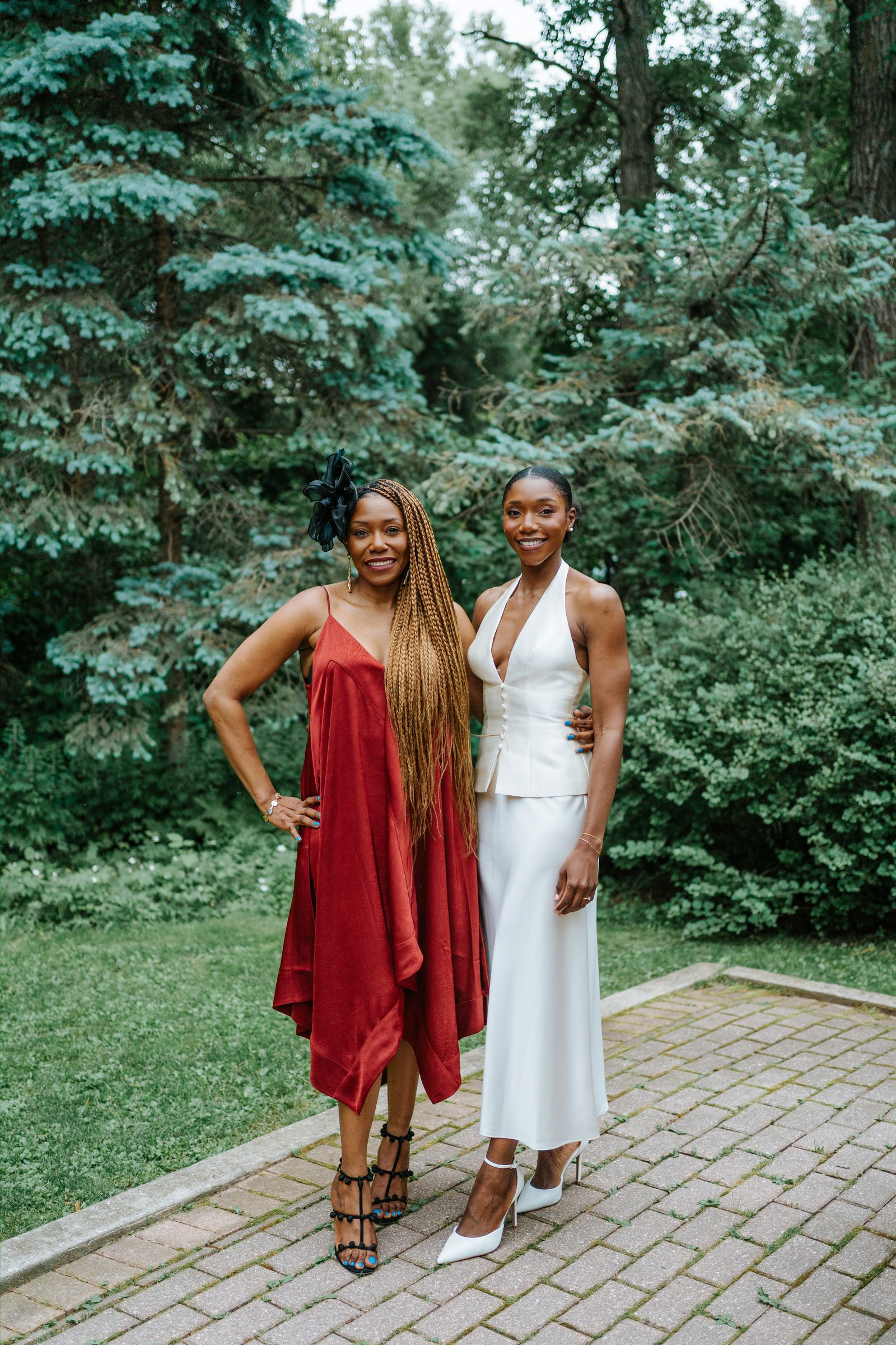 Tobi and a family member — a woman in a flowing red dress with long braids and a black fascinator — together at Leo Mol Sculpture Garden in Assiniboine Park, Winnipeg