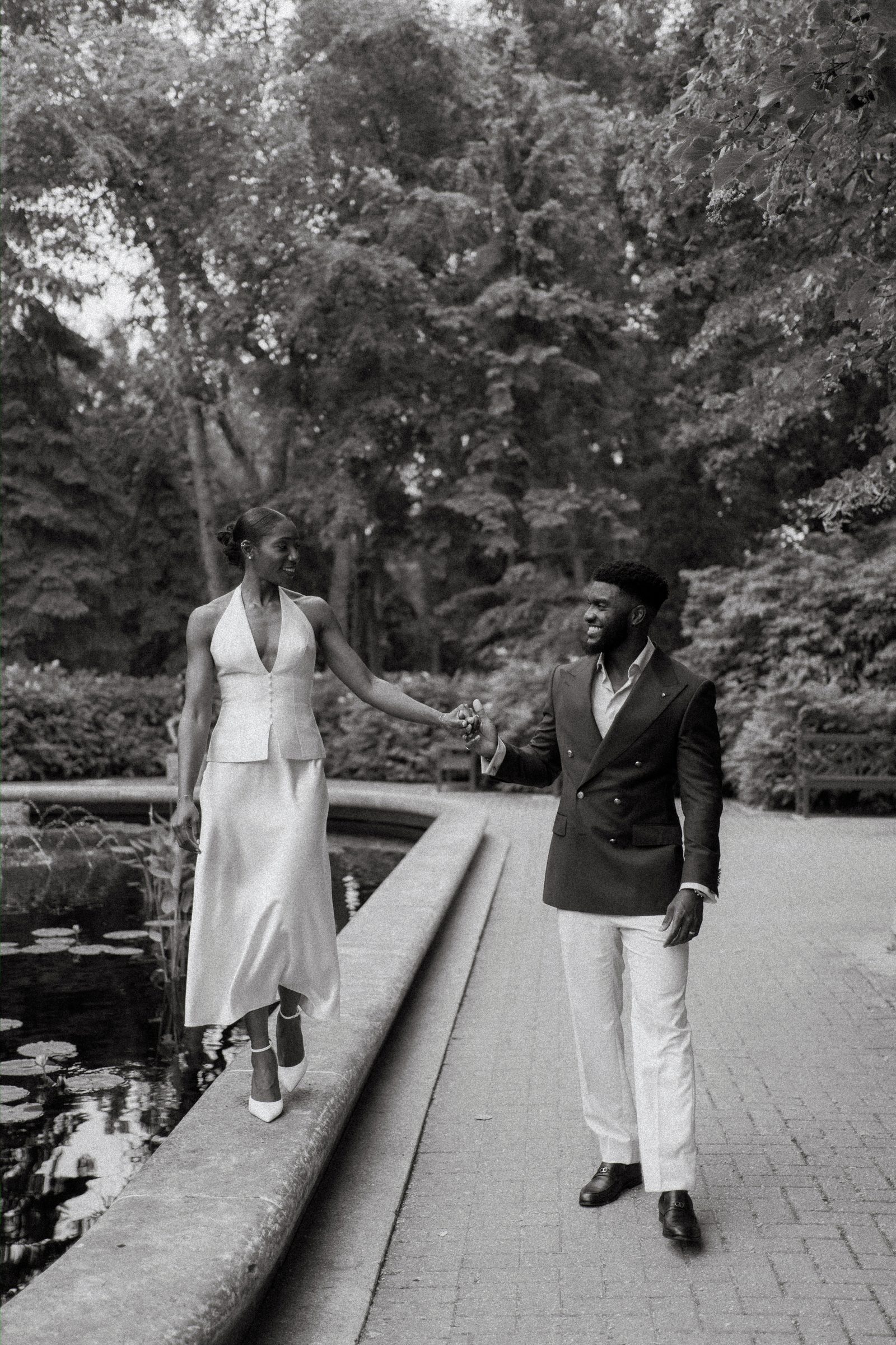 Emeka and Tobi walking together beside the lily pond at Leo Mol Sculpture Garden — garden portrait, Assiniboine Park, Winnipeg