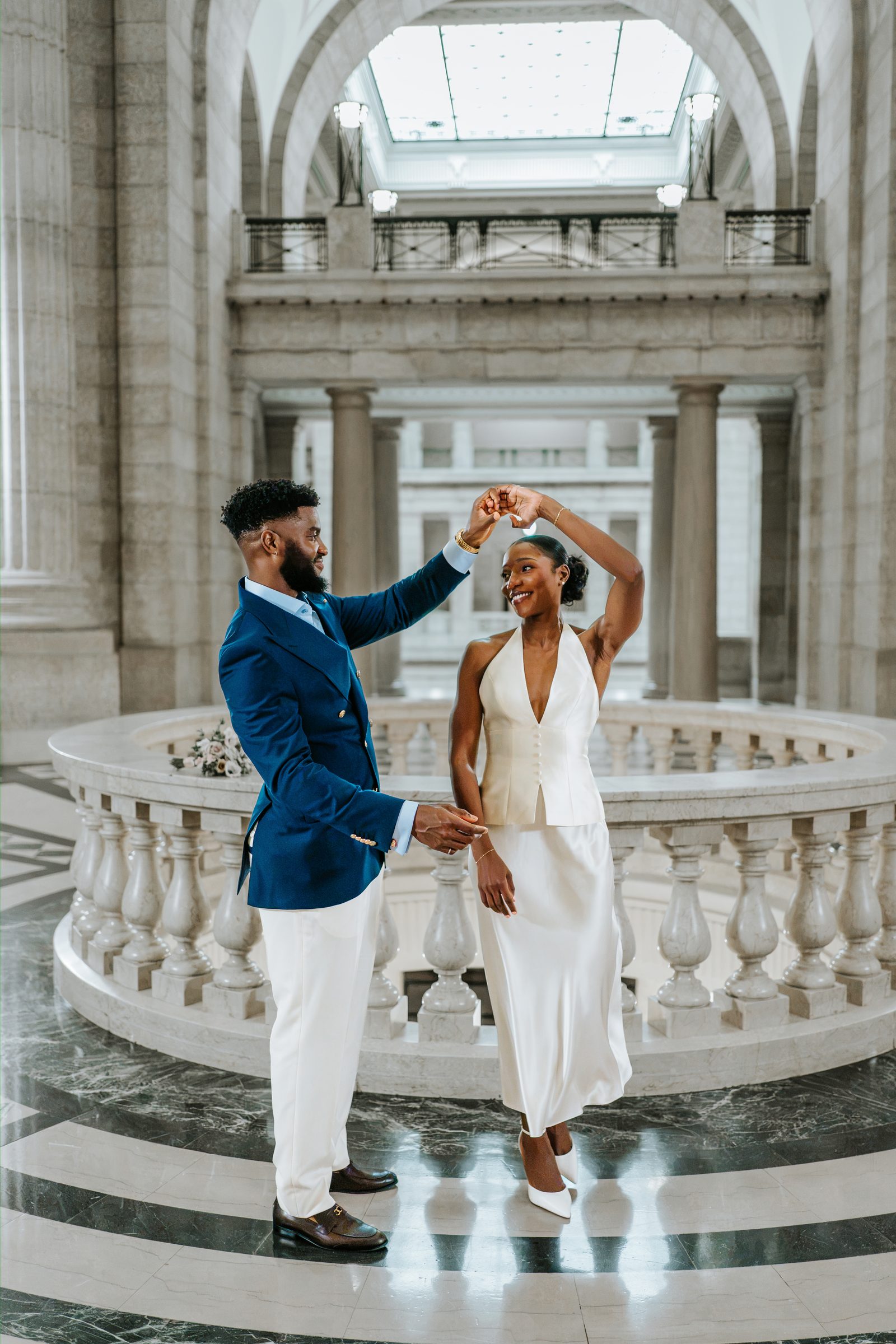 Emeka seated on the exterior marble steps of the Manitoba Legislative Building, Tobi standing behind — editorial couple portrait, Winnipeg wedding photographer Chris Ngo